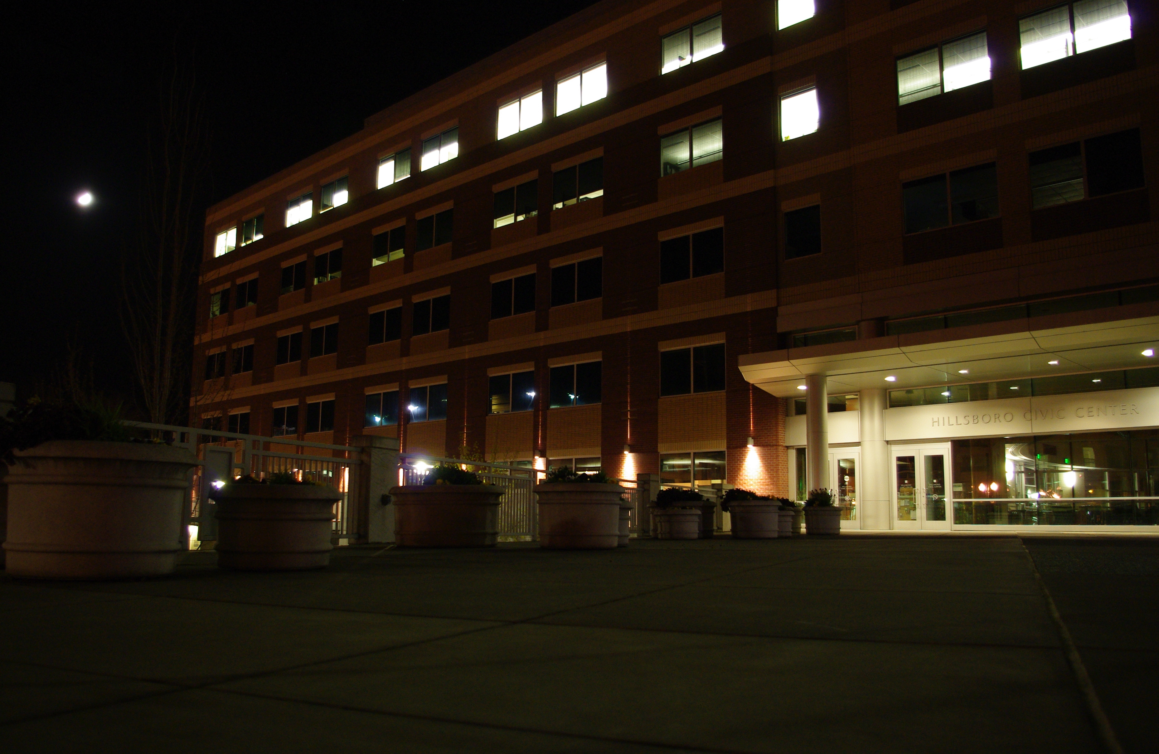 Multi-story brick municipal building at night with illuminated windows and entrance.