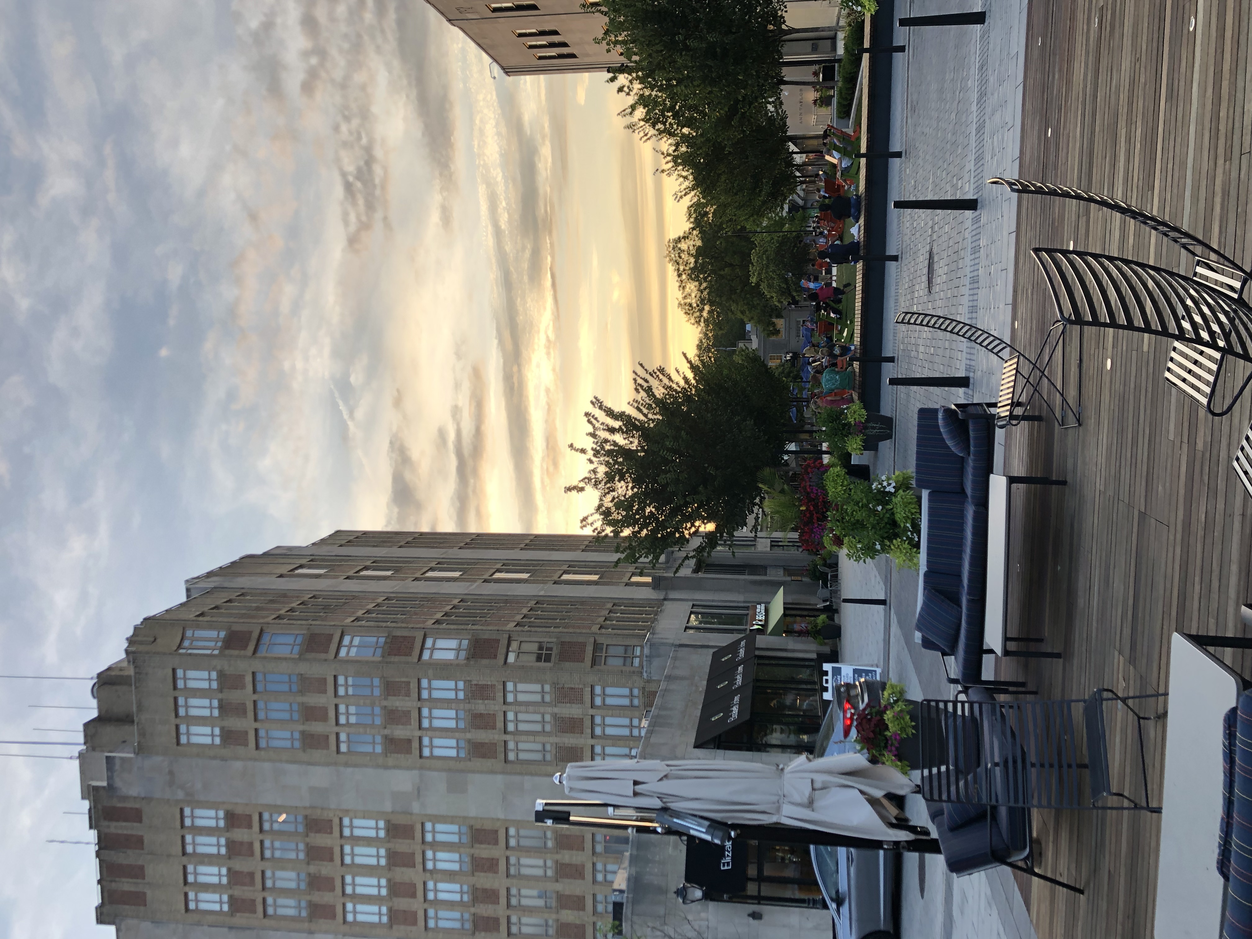 Outdoor pedestrian plaza with seating, trees, and a tall commercial building at dusk.