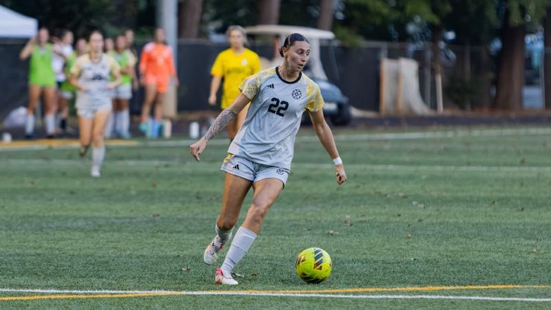 Female soccer player in white jersey number 22 dribbling a yellow ball on turf.