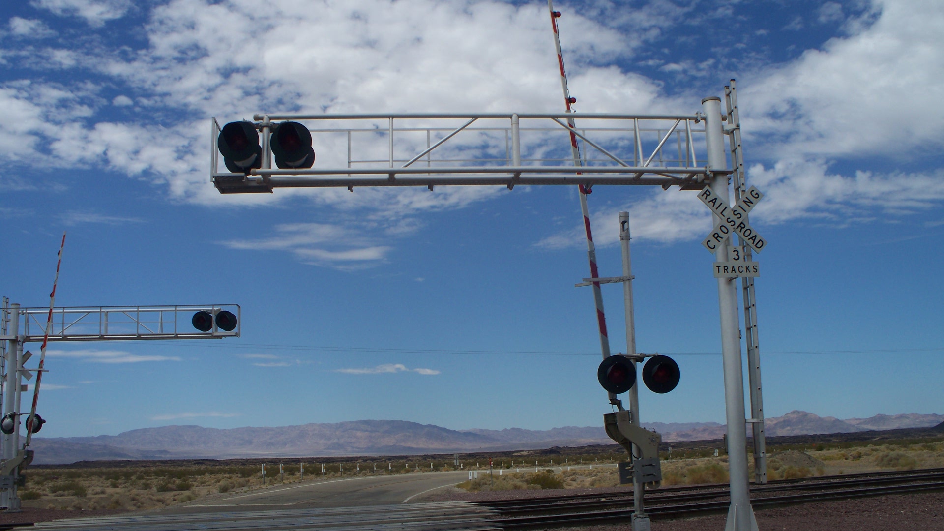 BNSF railroad crossing with overhead signal gantries and flashing warning lights.