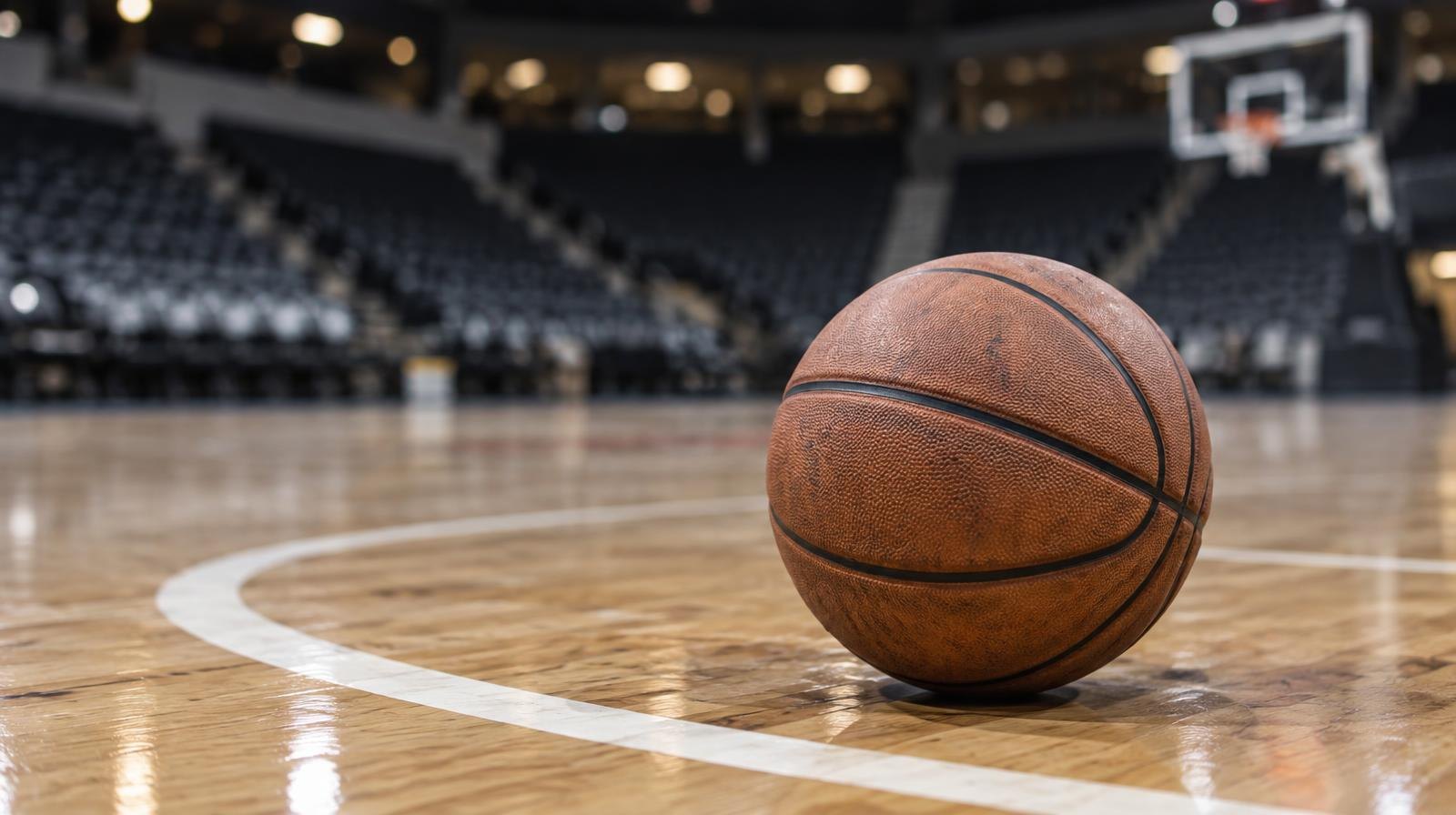 A basketball resting on a hardwood court floor near the three-point arc.