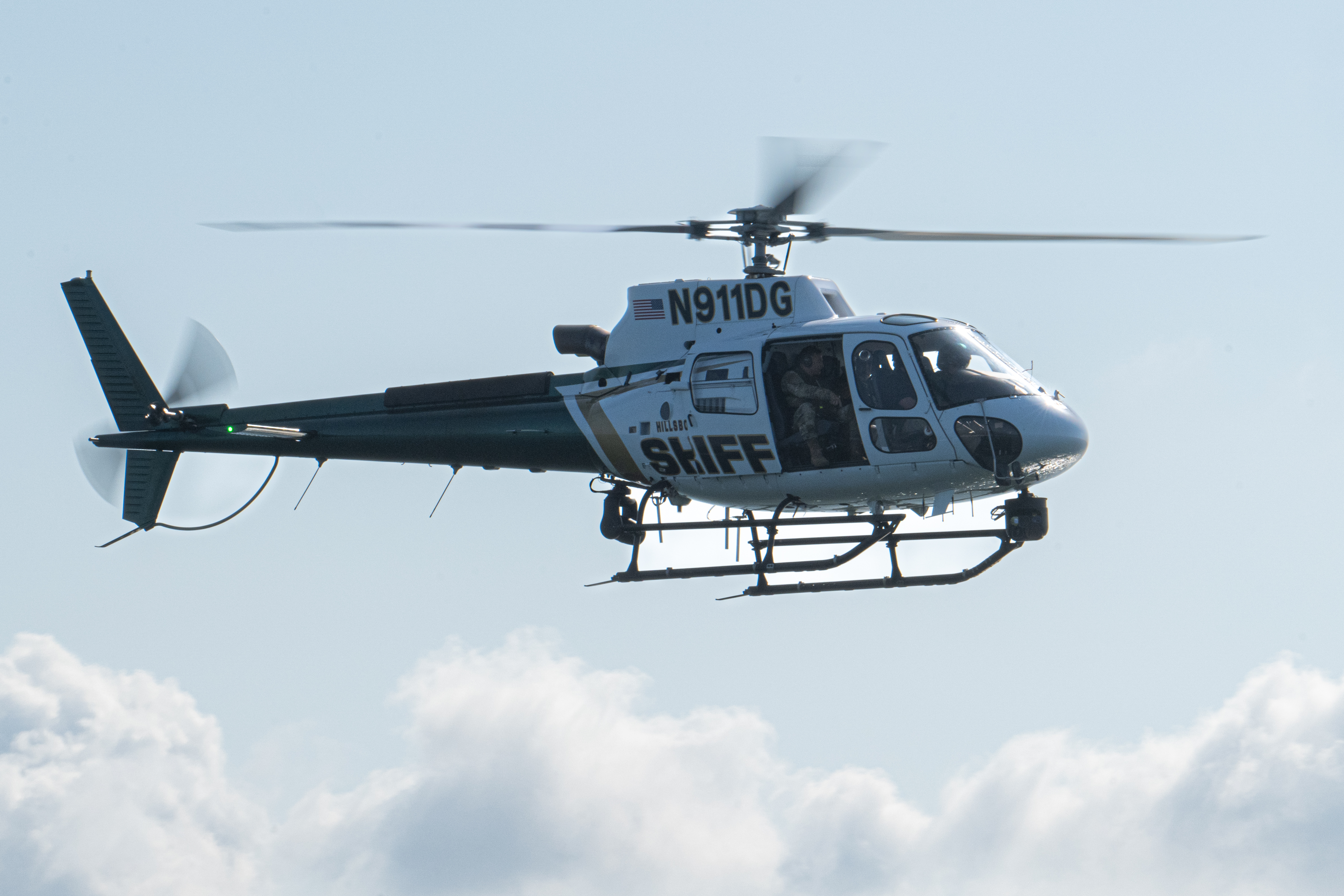 A white helicopter marked SHERIFF in flight against a partly cloudy sky.