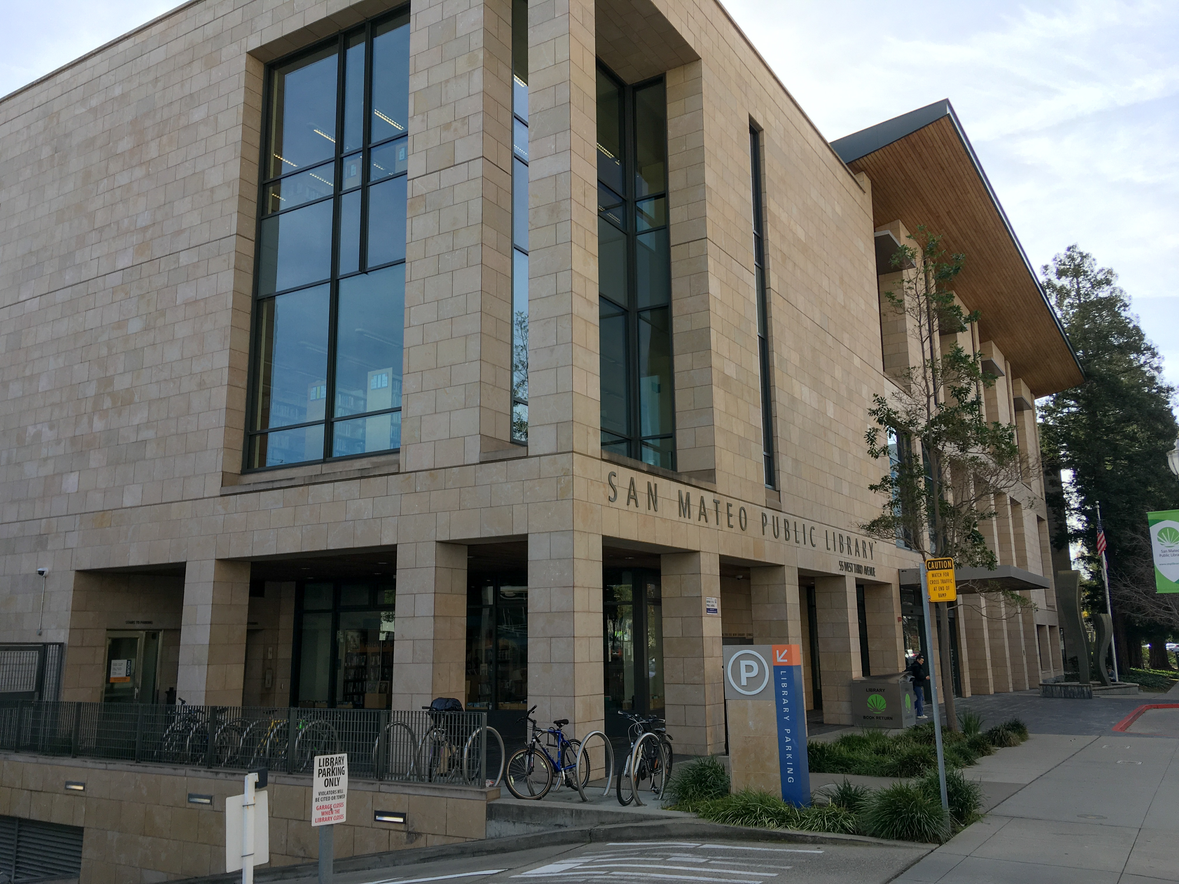 Modern stone and glass public library building with bicycles parked out front.