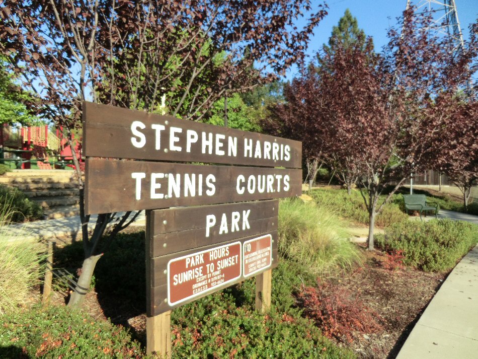 Wooden park entrance sign surrounded by trees and landscaped shrubs.
