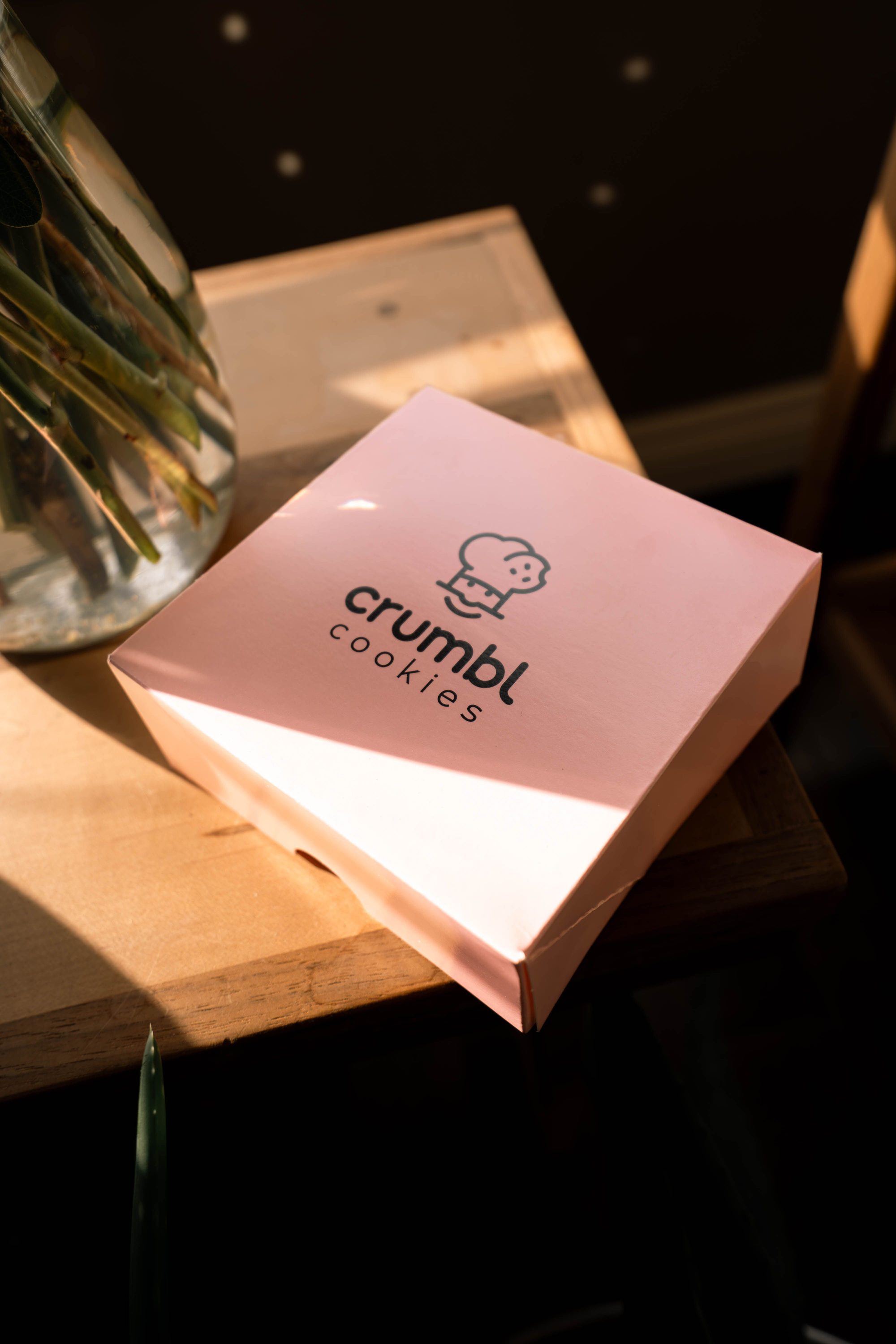 Pink Crumbl Cookies box on a sunlit table indoors, perfect for dessert lovers.