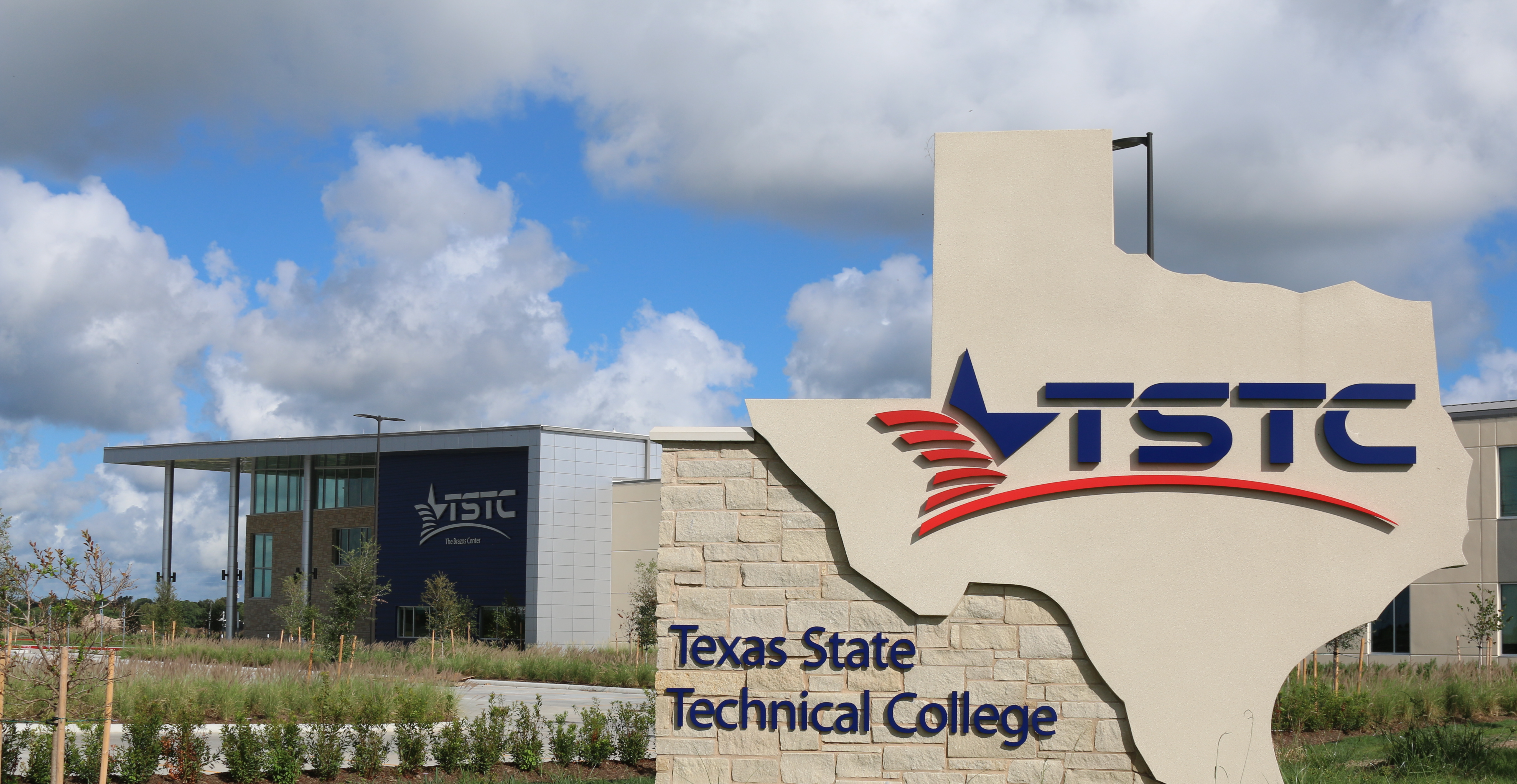 Stone monument sign shaped like Texas with TSTC logo in front of a campus building