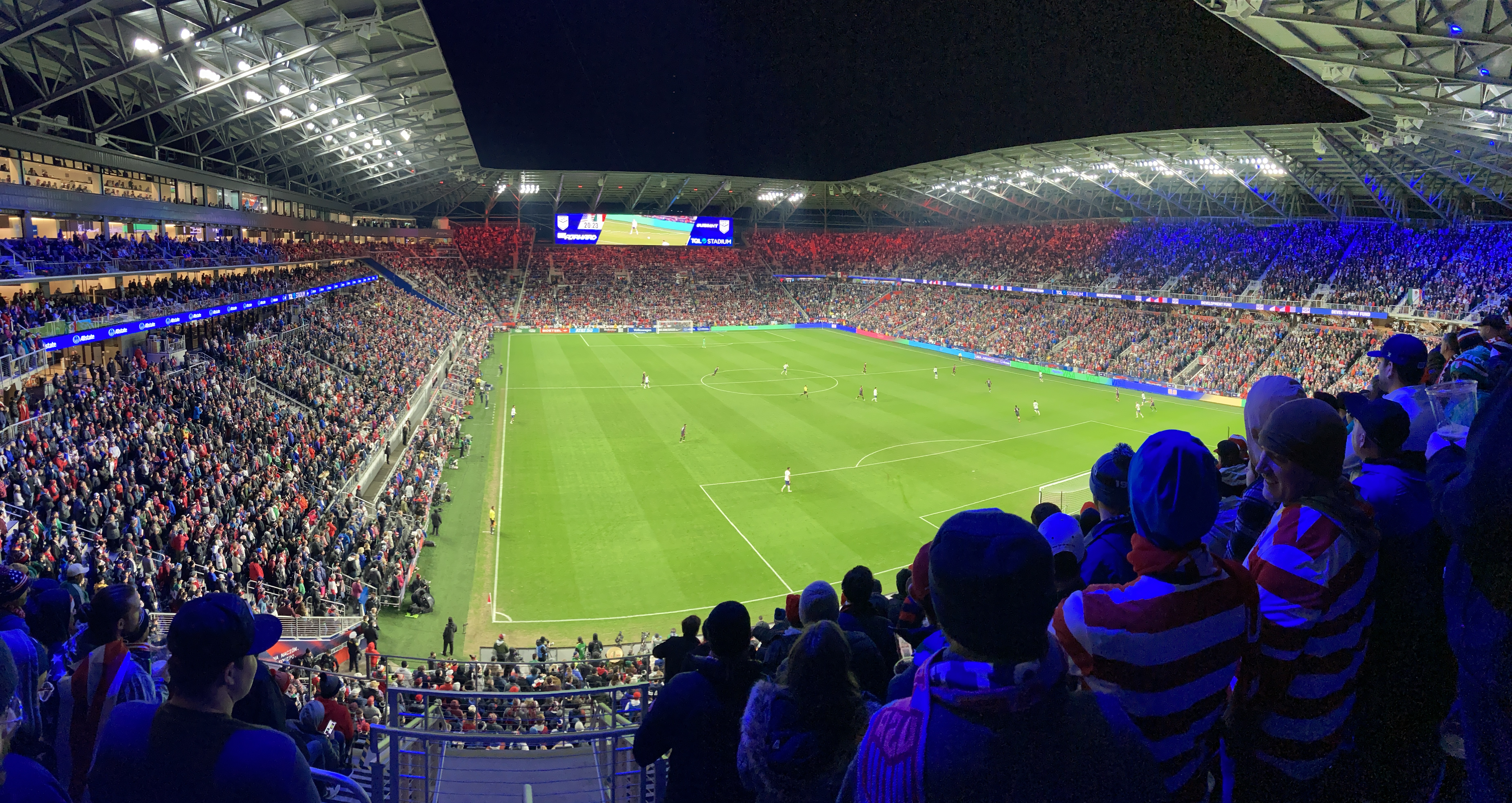 Packed soccer stadium at night with a bright green pitch and full stands