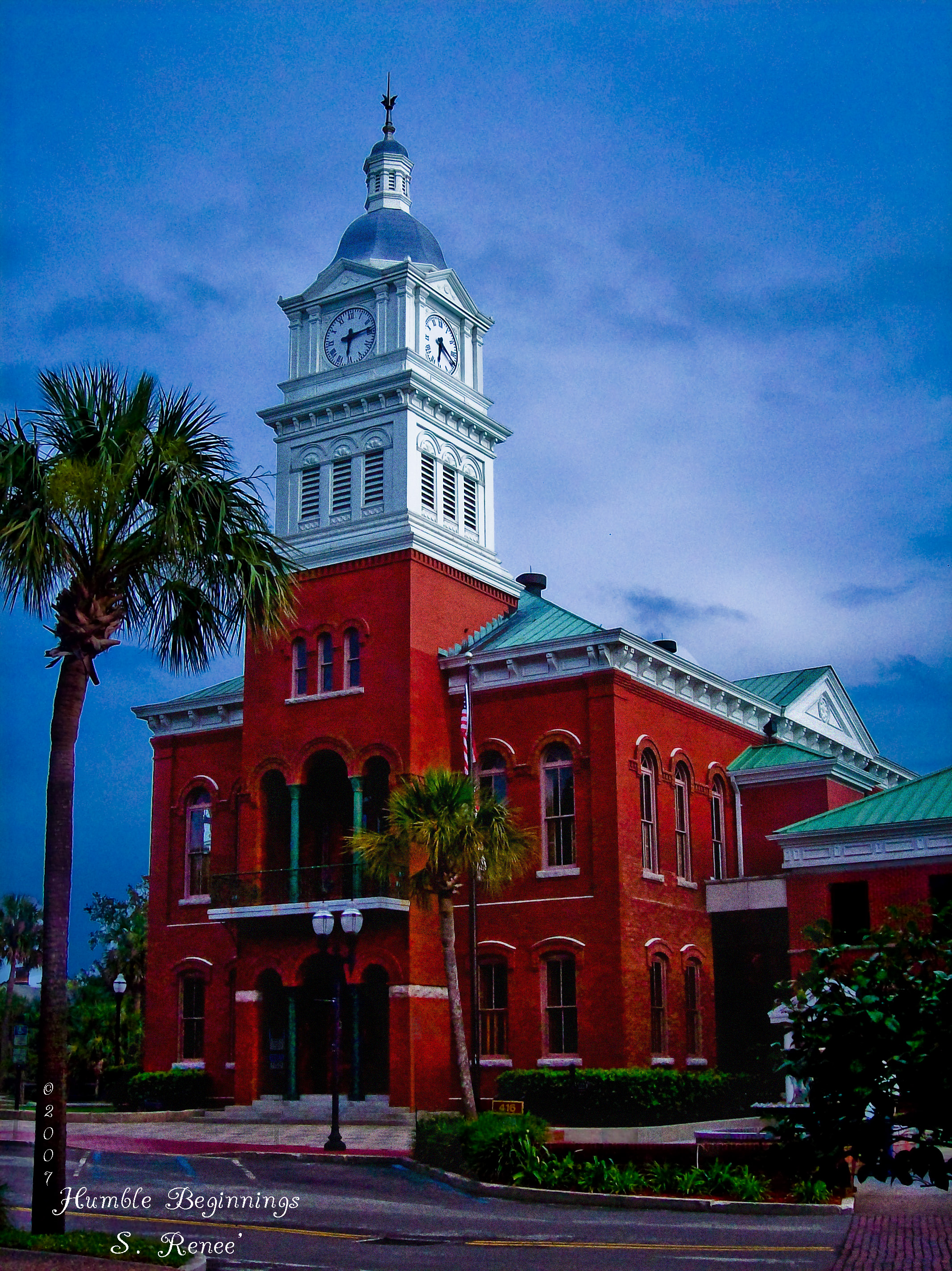 Red brick historic courthouse with white clock tower flanked by palm trees.