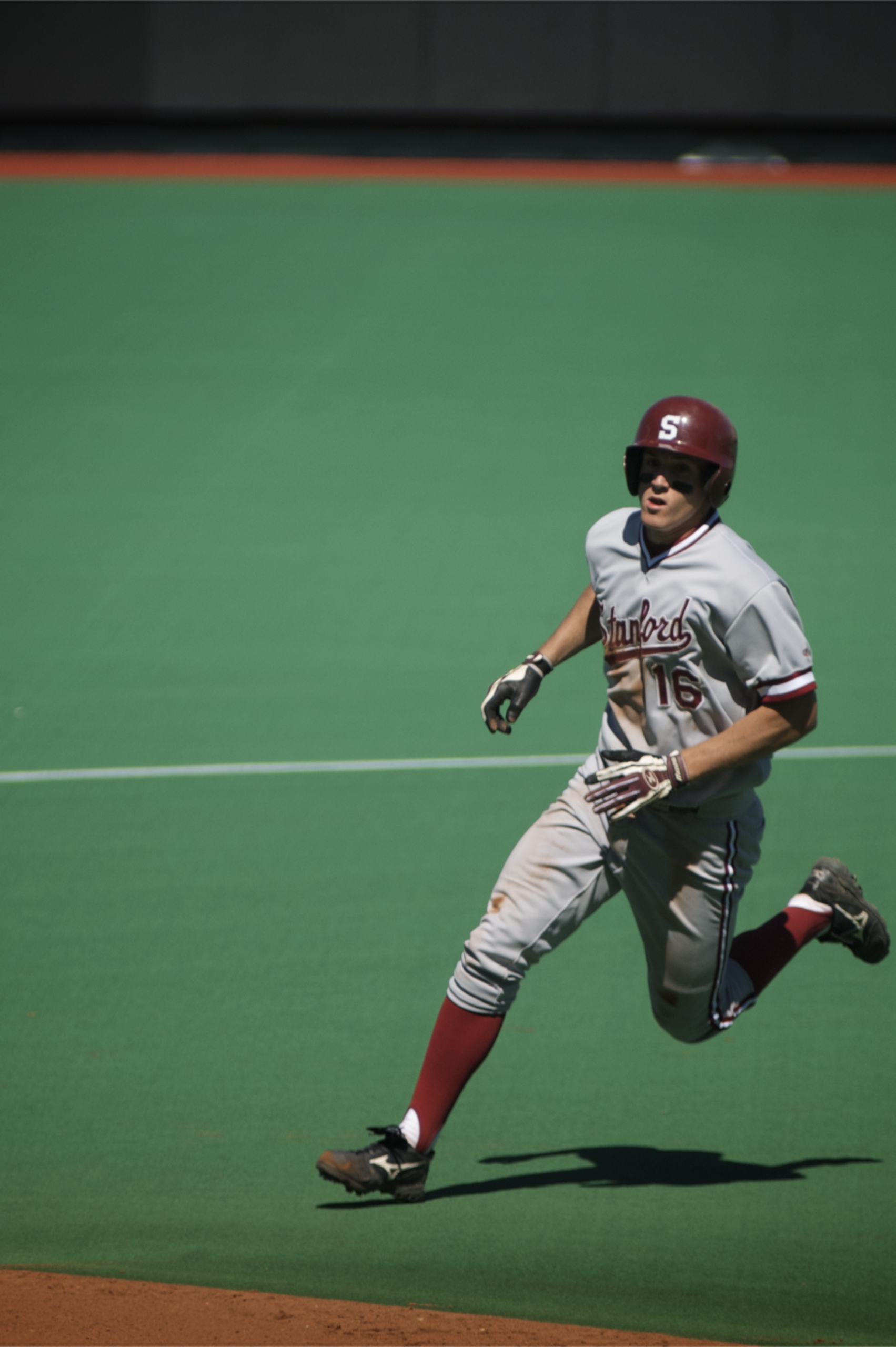 A baseball player in a gray Stanford uniform and red socks running on the basepath.