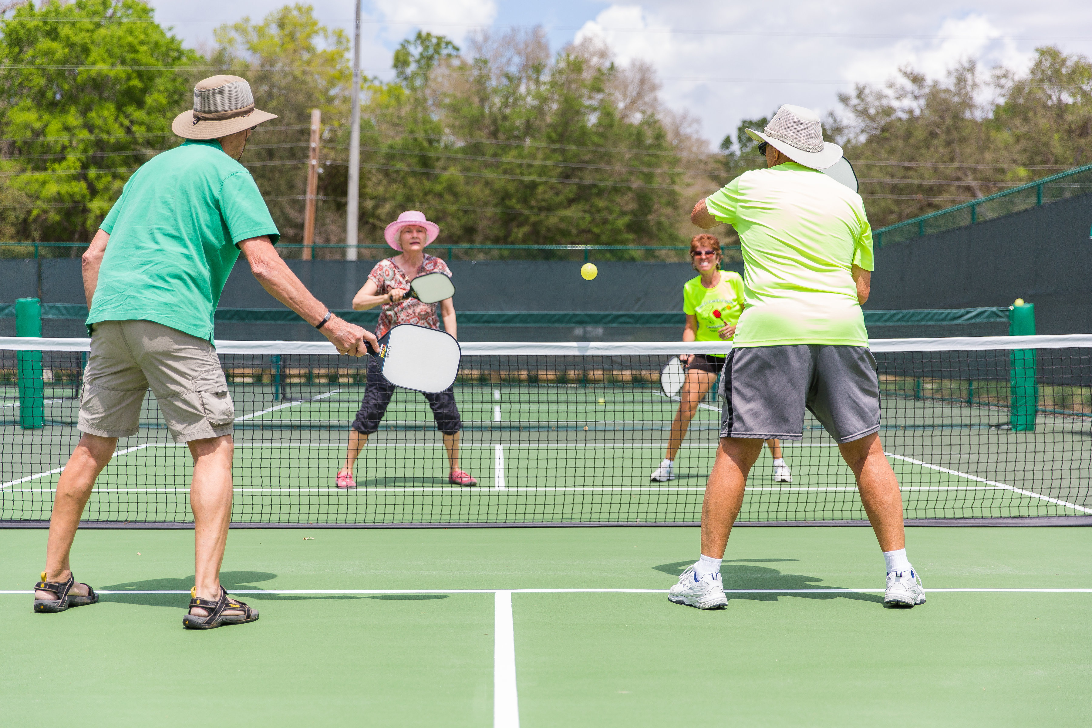 Four adults playing doubles pickleball on a green outdoor court.
