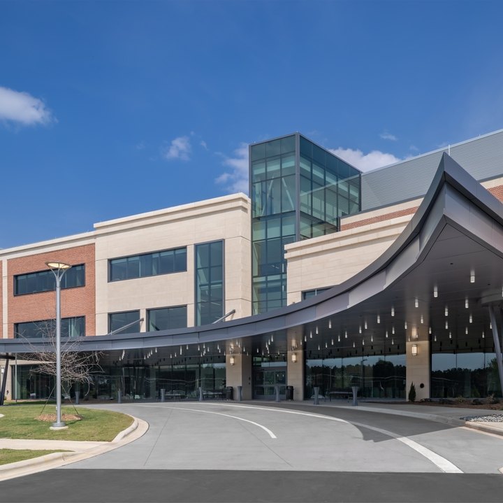 Modern multi-story hospital building with curved canopy entrance and circular driveway.