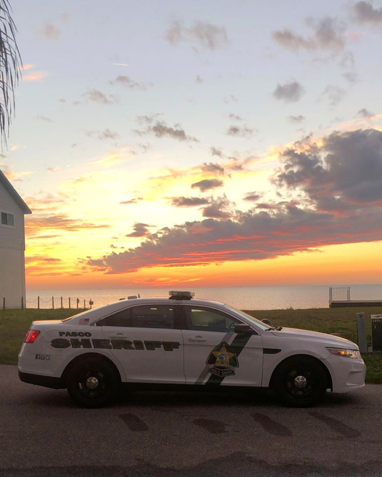 White Pasco County Sheriff's Office patrol car parked outdoors at sunset near water.