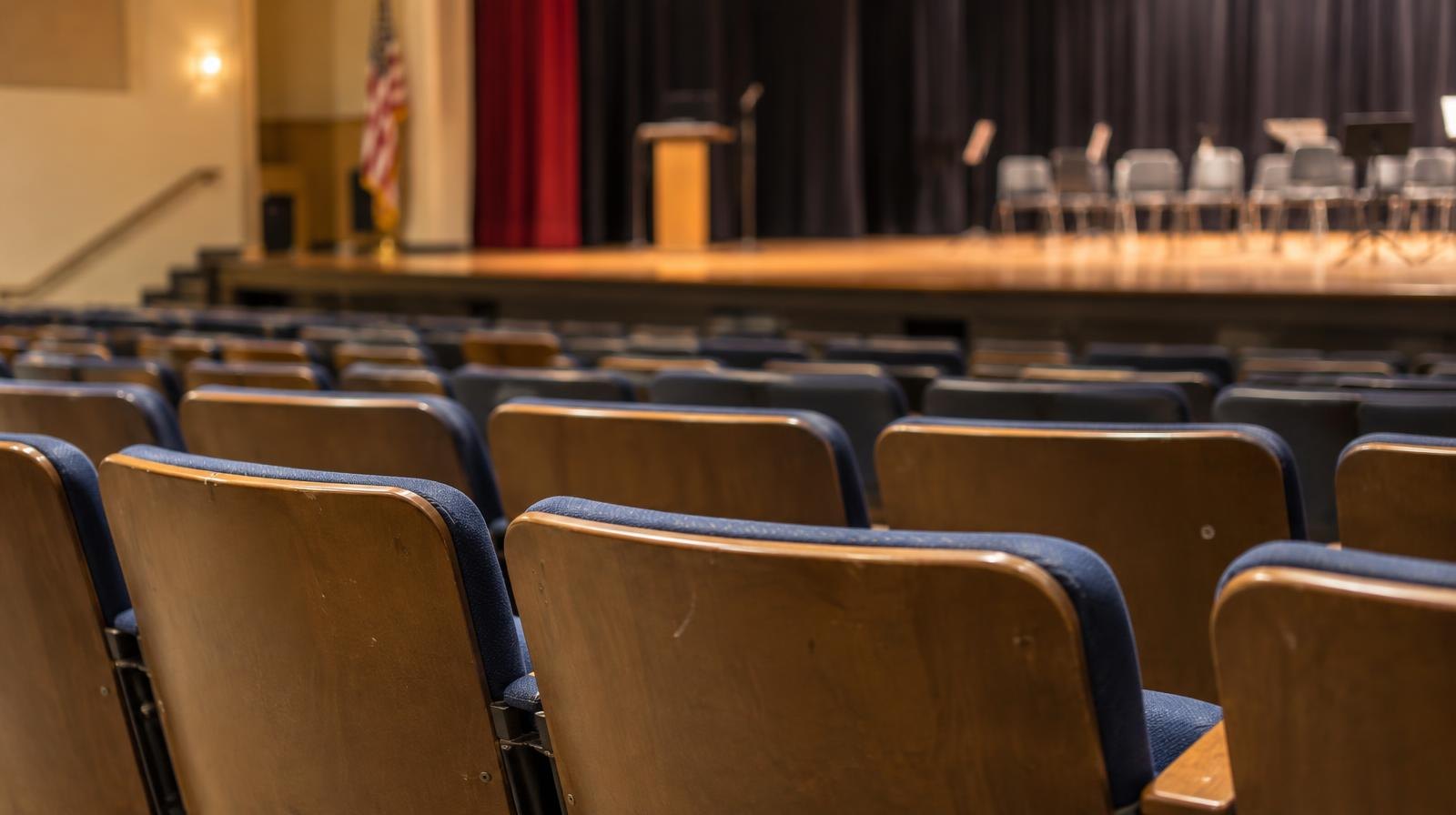 Rows of empty auditorium seats facing a lit stage.