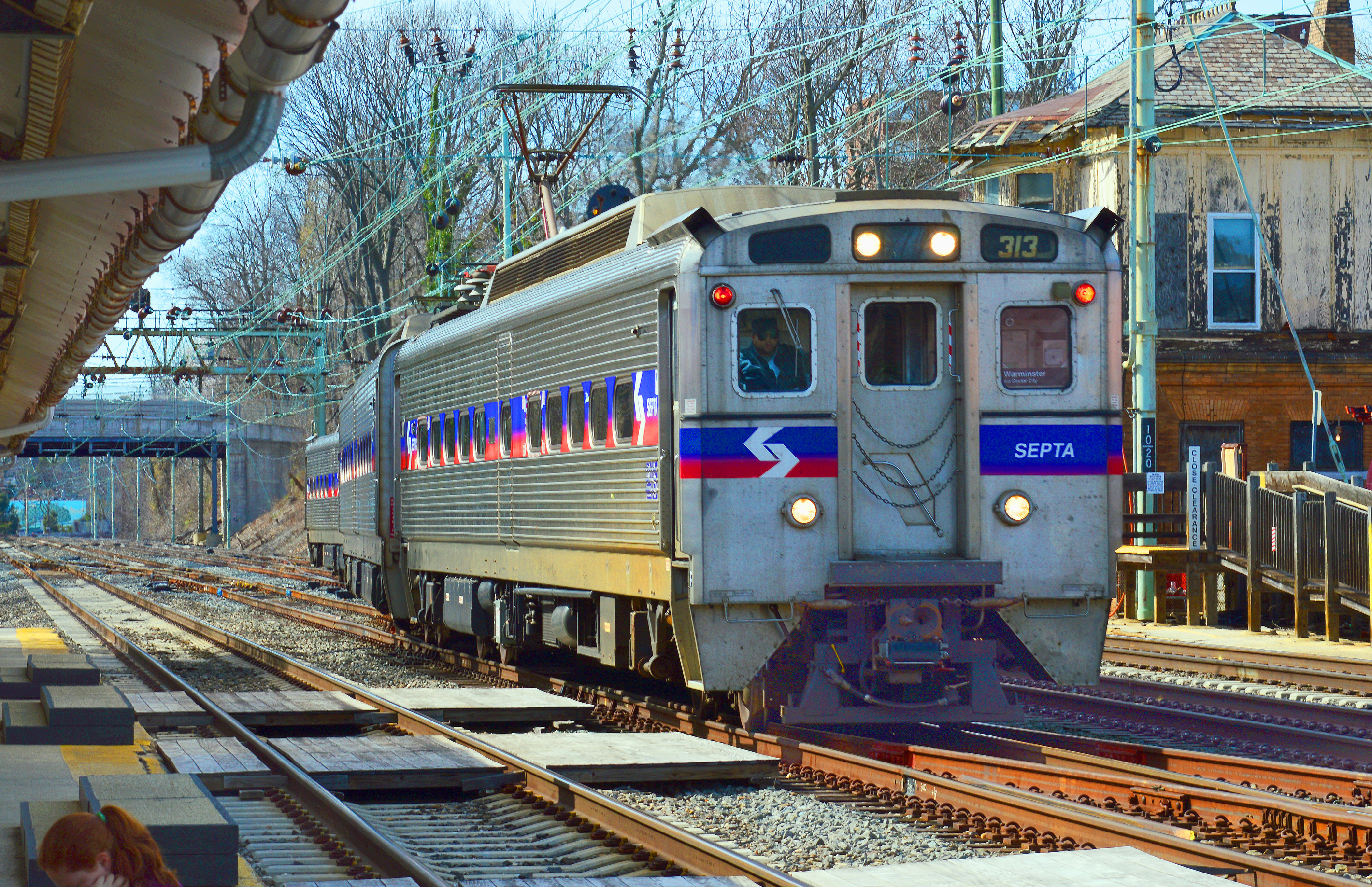 Silver SEPTA commuter rail cars on electrified tracks at a station platform.