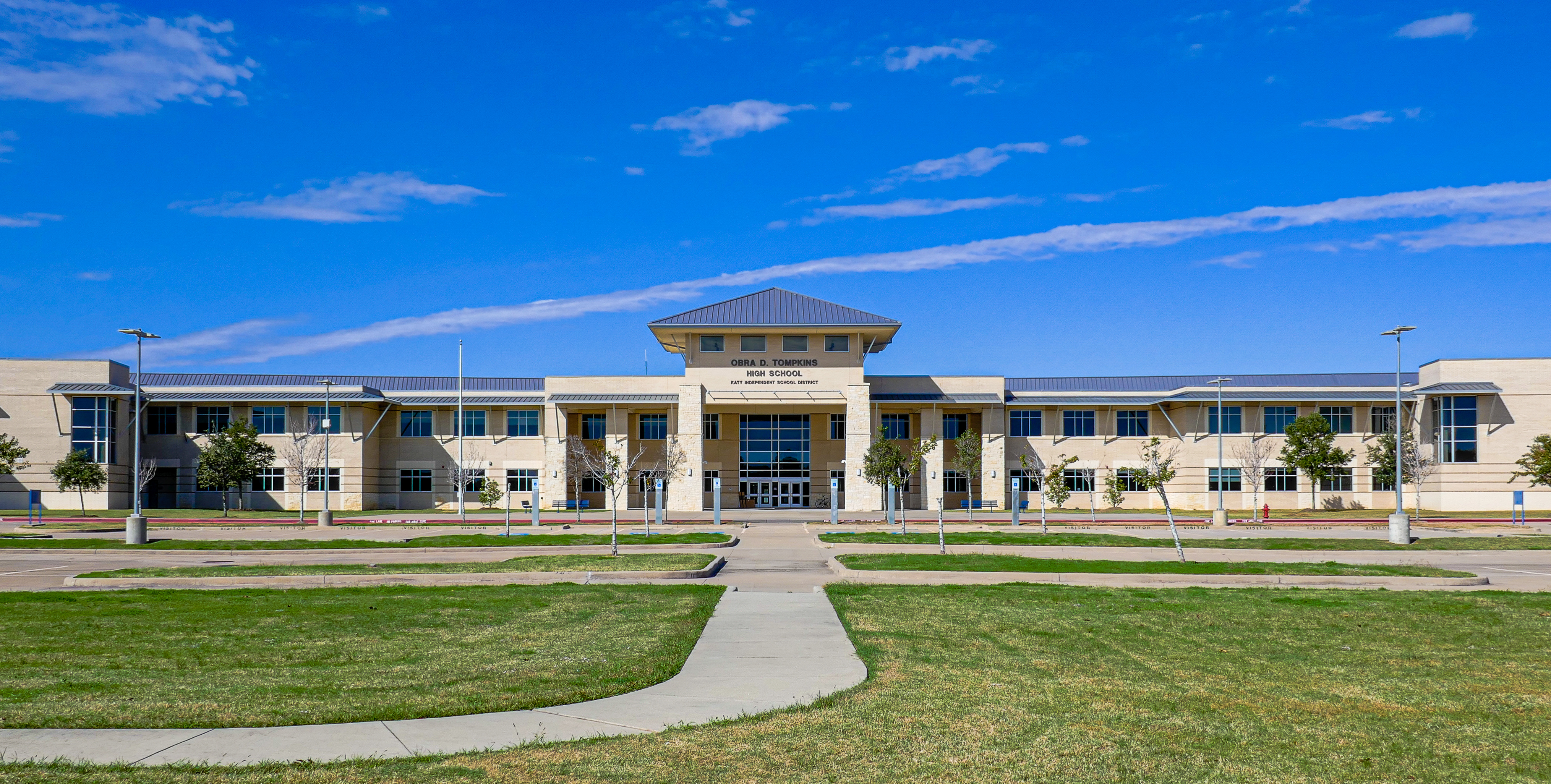 Two-story school building with green lawn and curved walkways under a blue sky.