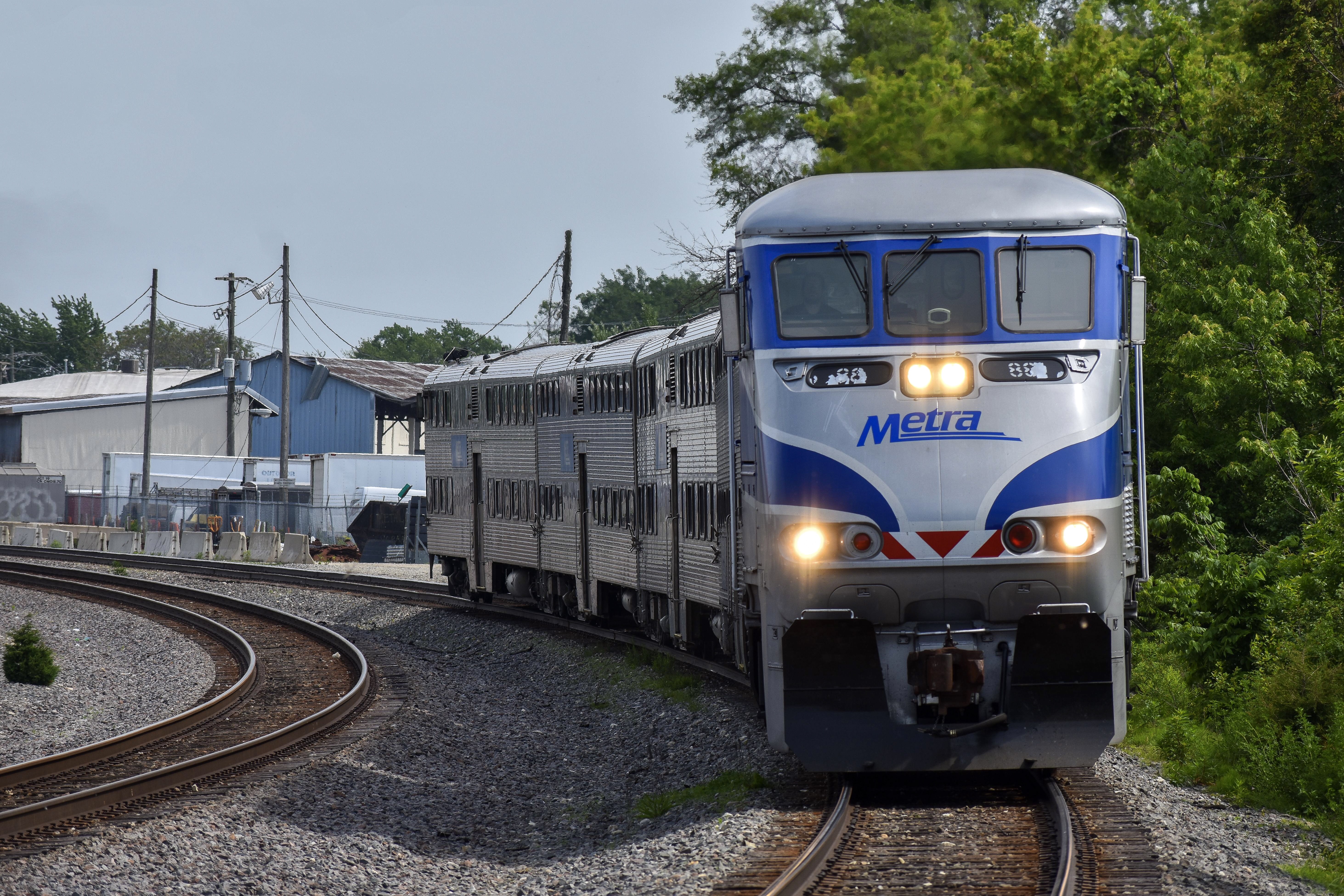 A Metra commuter train with headlights on travels along a curved suburban track.