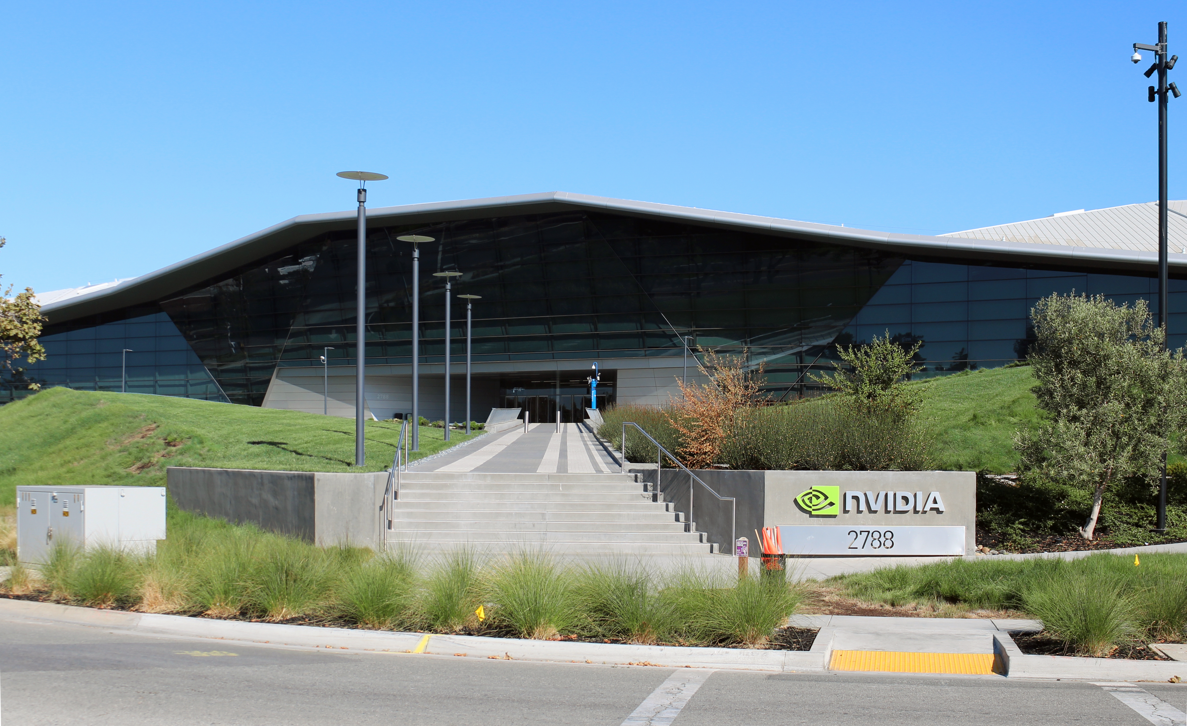 Modern angular glass building with Nvidia logo sign in front, surrounded by green landscaping.