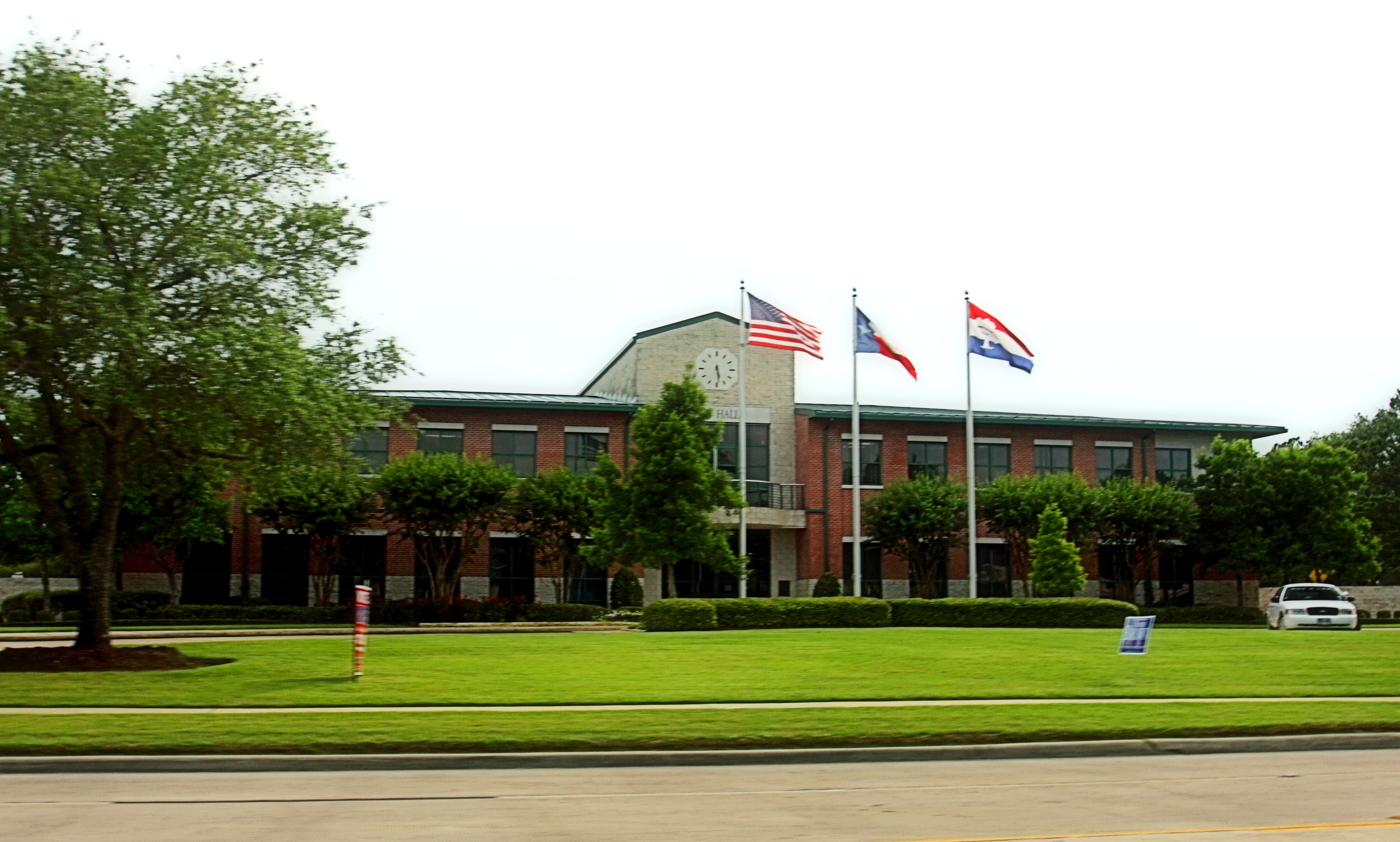Two-story red brick city hall with green metal roof and three flagpoles out front.