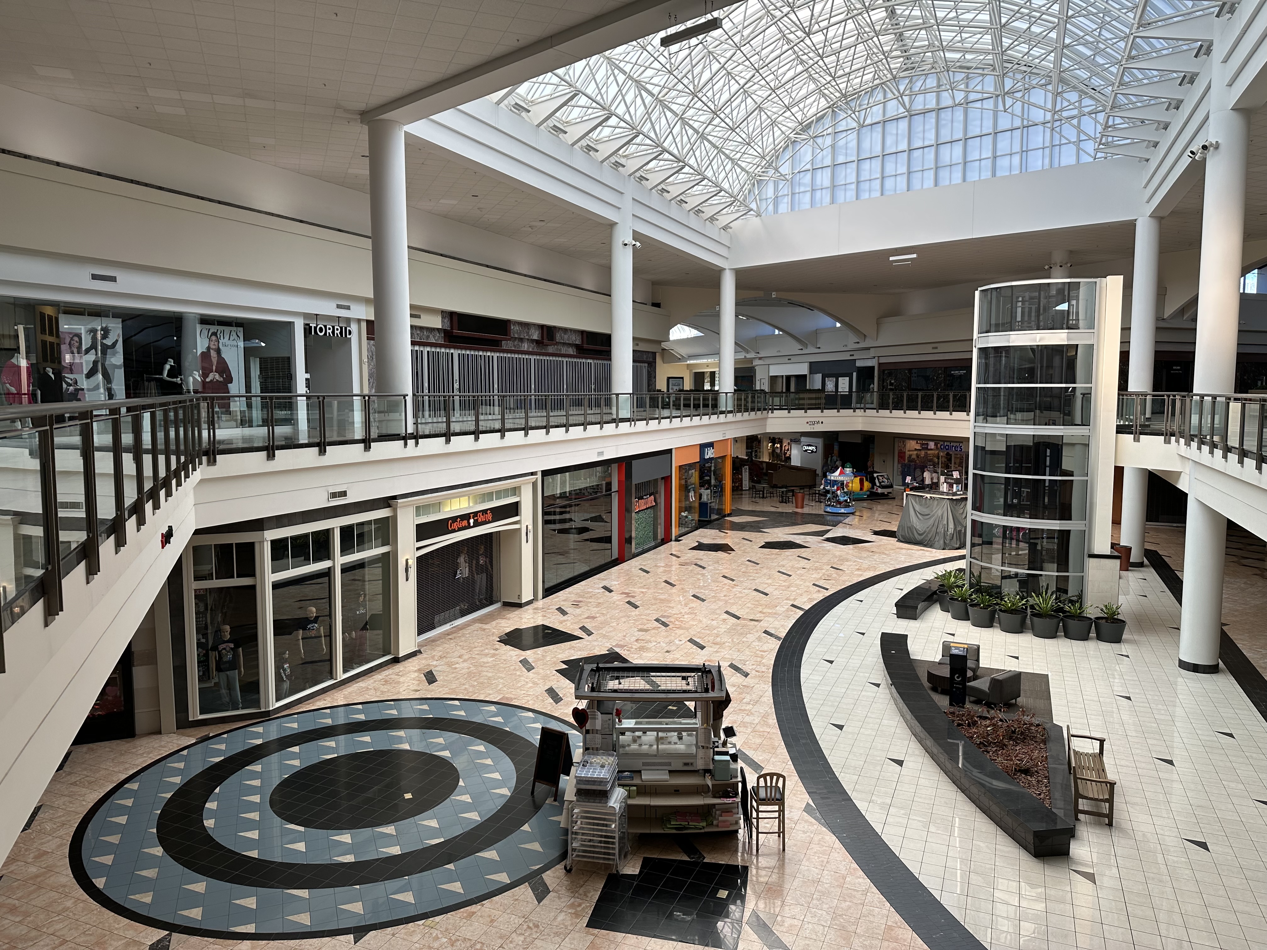 Two-story mall interior with mostly empty storefronts and a skylight atrium.