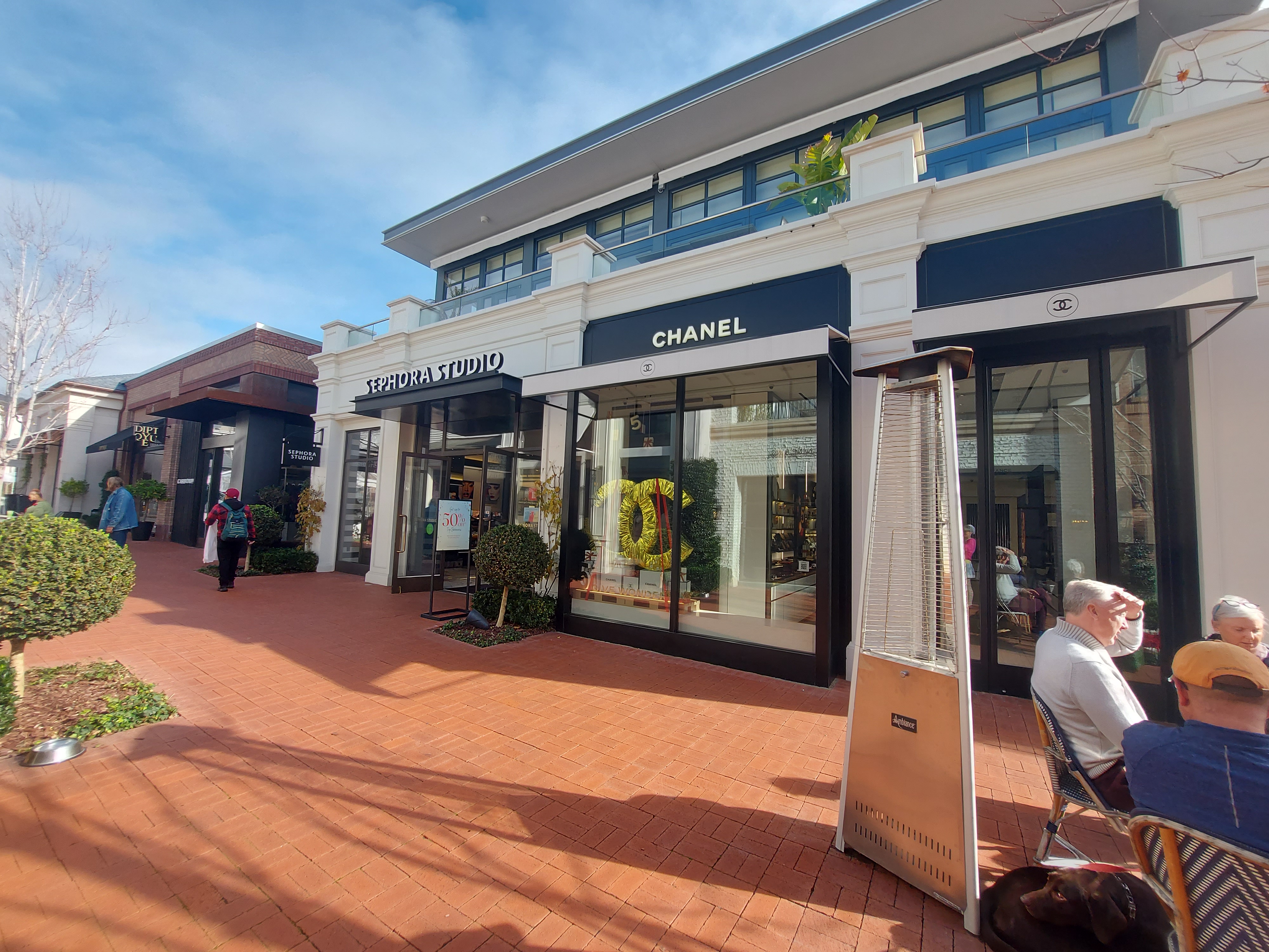 Brick-paved pedestrian walkway at an outdoor shopping center with storefronts and outdoor diners.