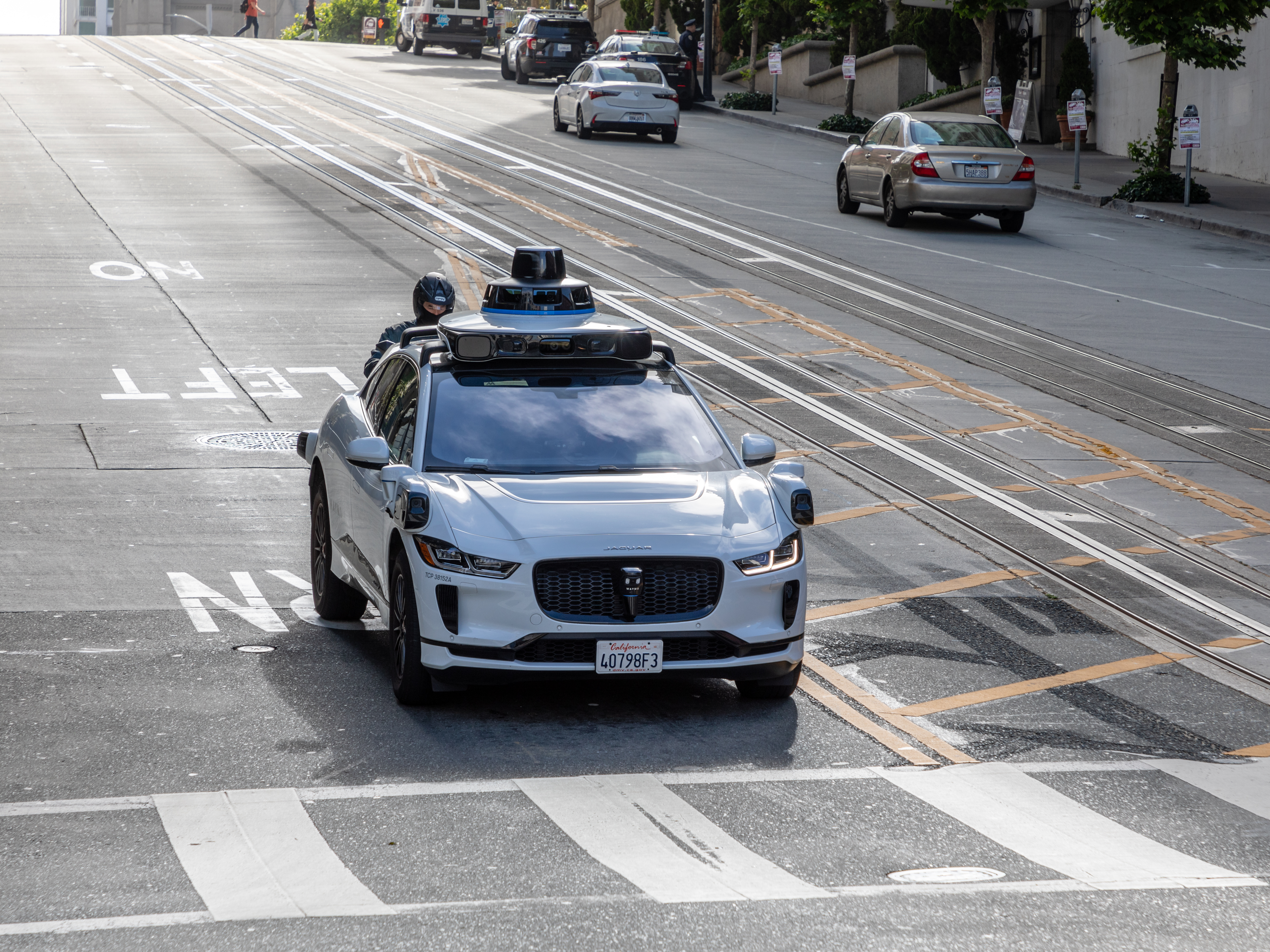 White Waymo autonomous vehicle with roof-mounted sensors on a city street.