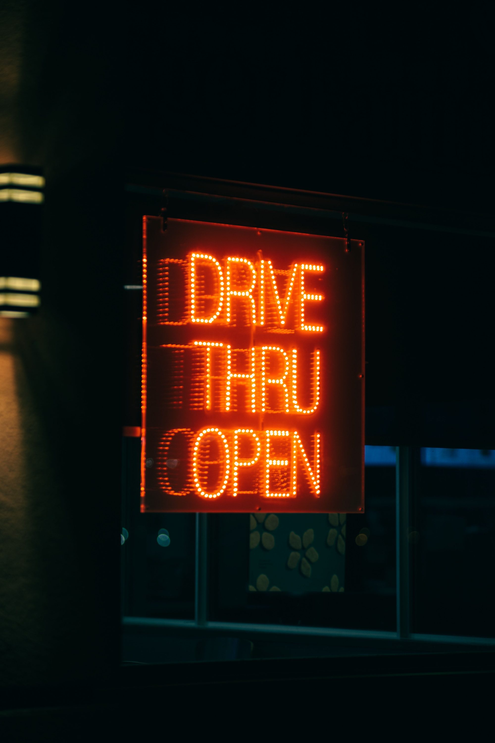 Glowing neon drive-thru sign illuminated against a dark background, indicating an open fast food service.