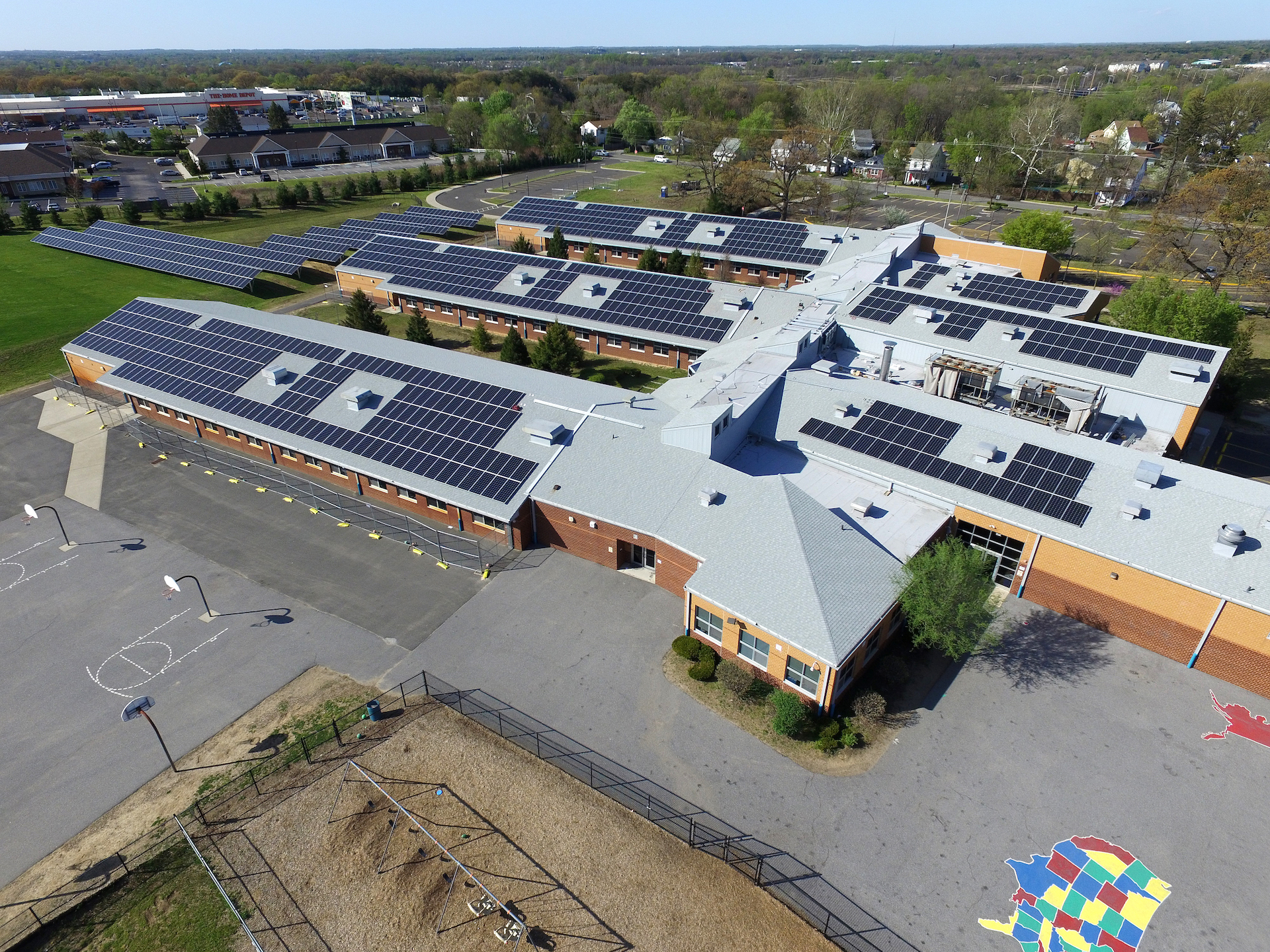 Aerial view of a school building with extensive rooftop solar panel arrays and surrounding grounds.
