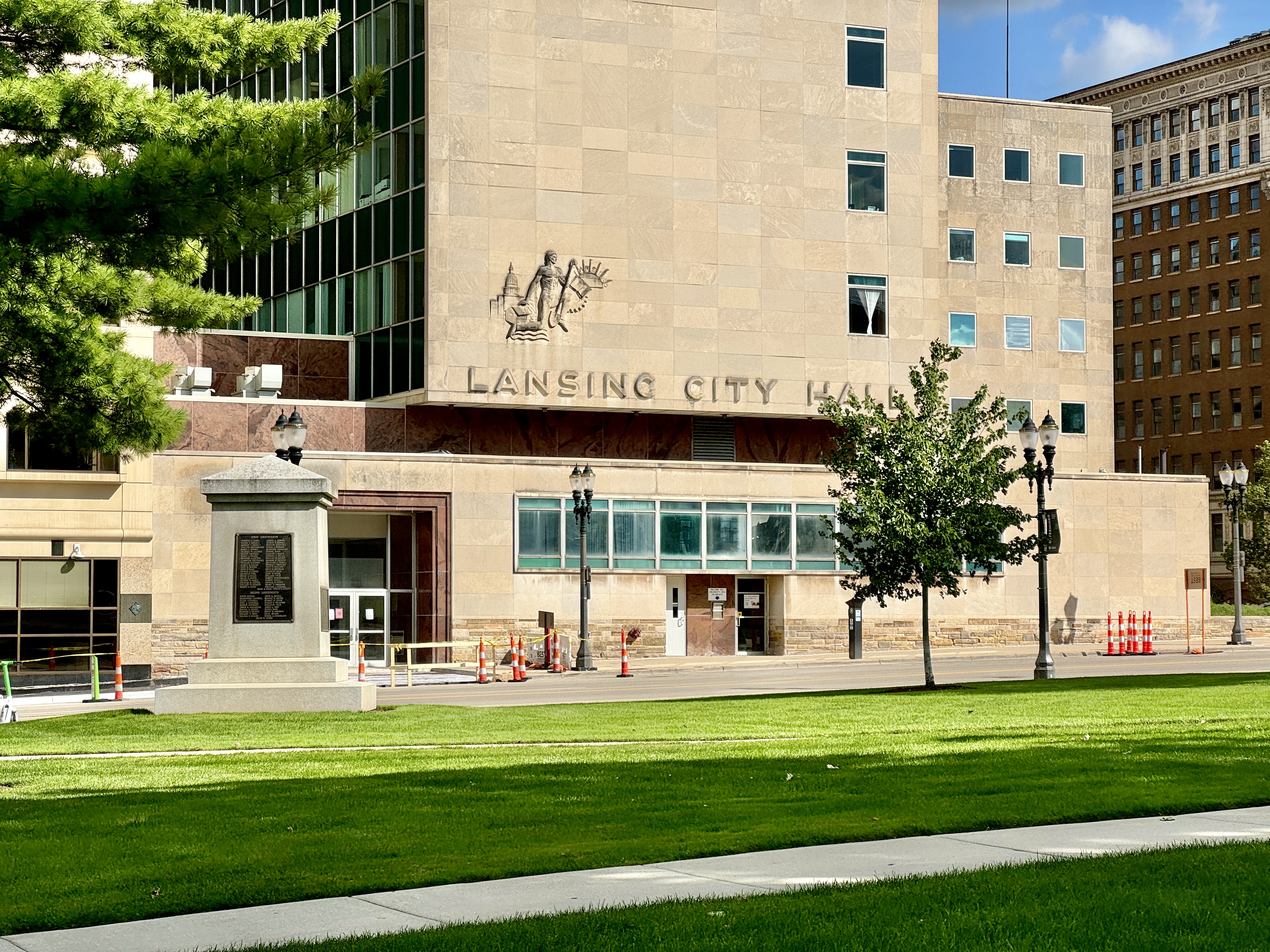 Exterior of Lansing City Hall with carved stone lettering and a small monument in front.