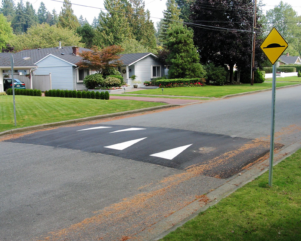 A residential street speed hump with white chevron markings and a yellow warning sign.