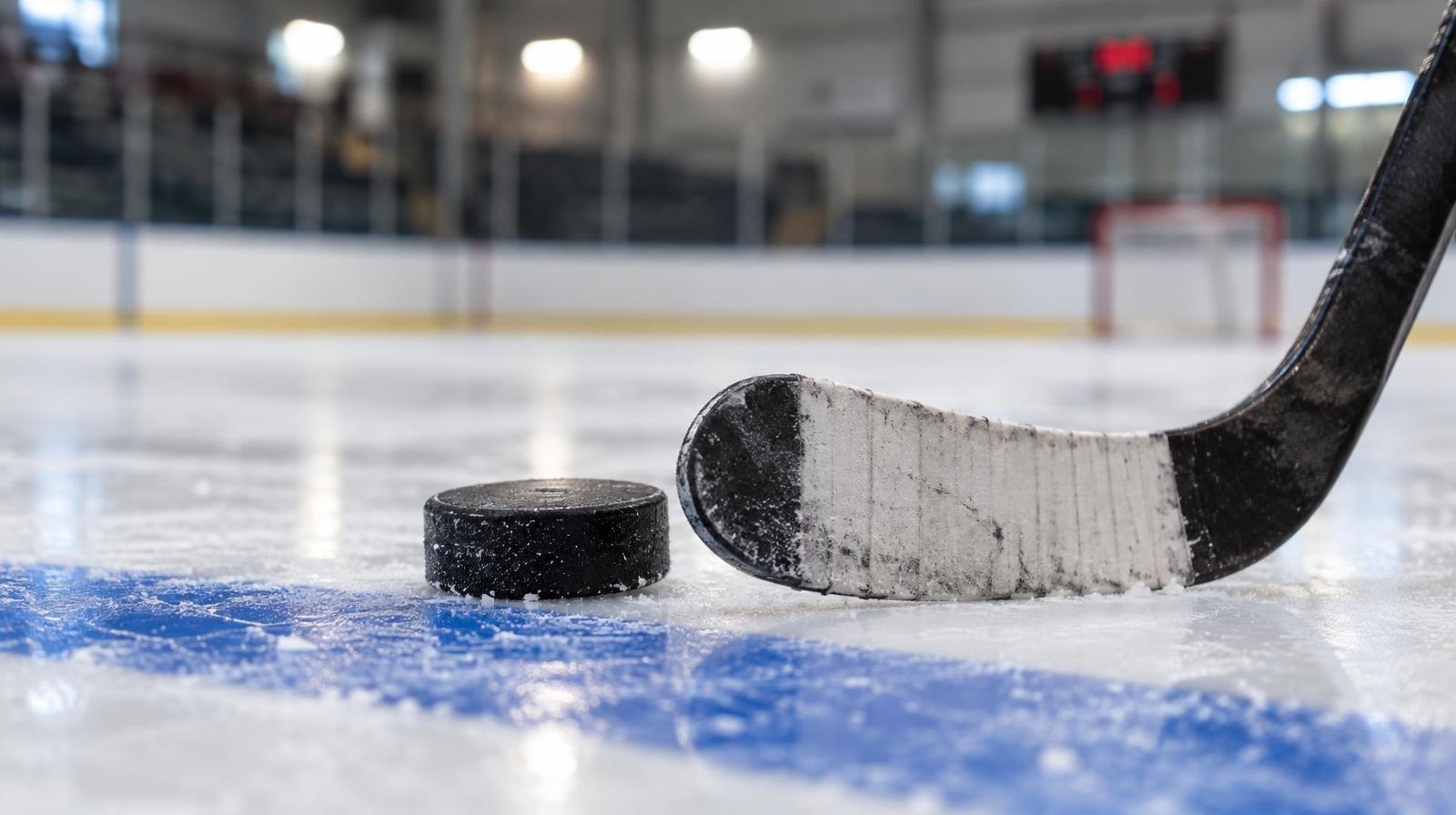 An ice hockey puck and stick blade resting on the ice near a blue line.