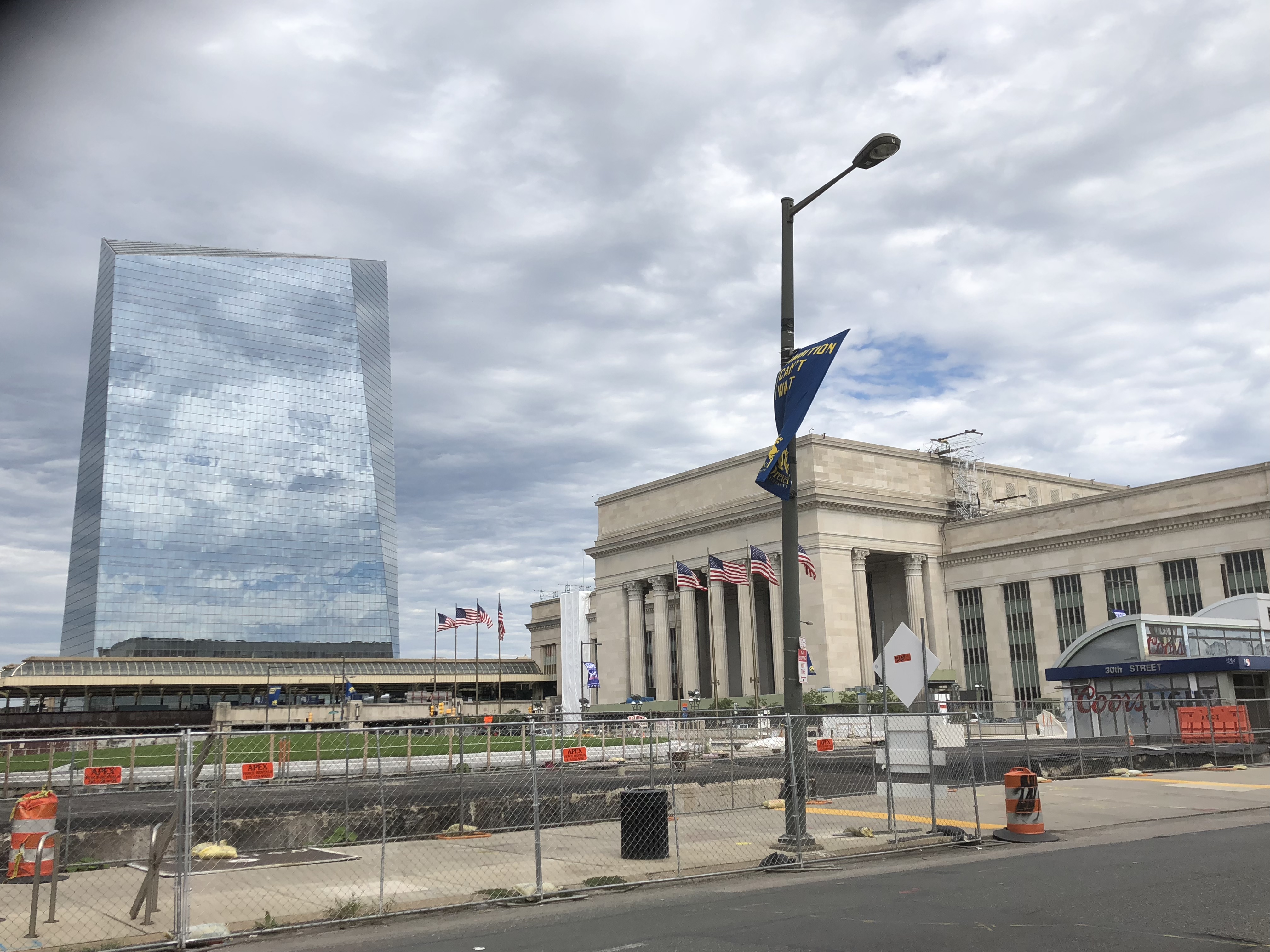 Classical stone train station and glass skyscraper in Philadelphia under overcast skies.