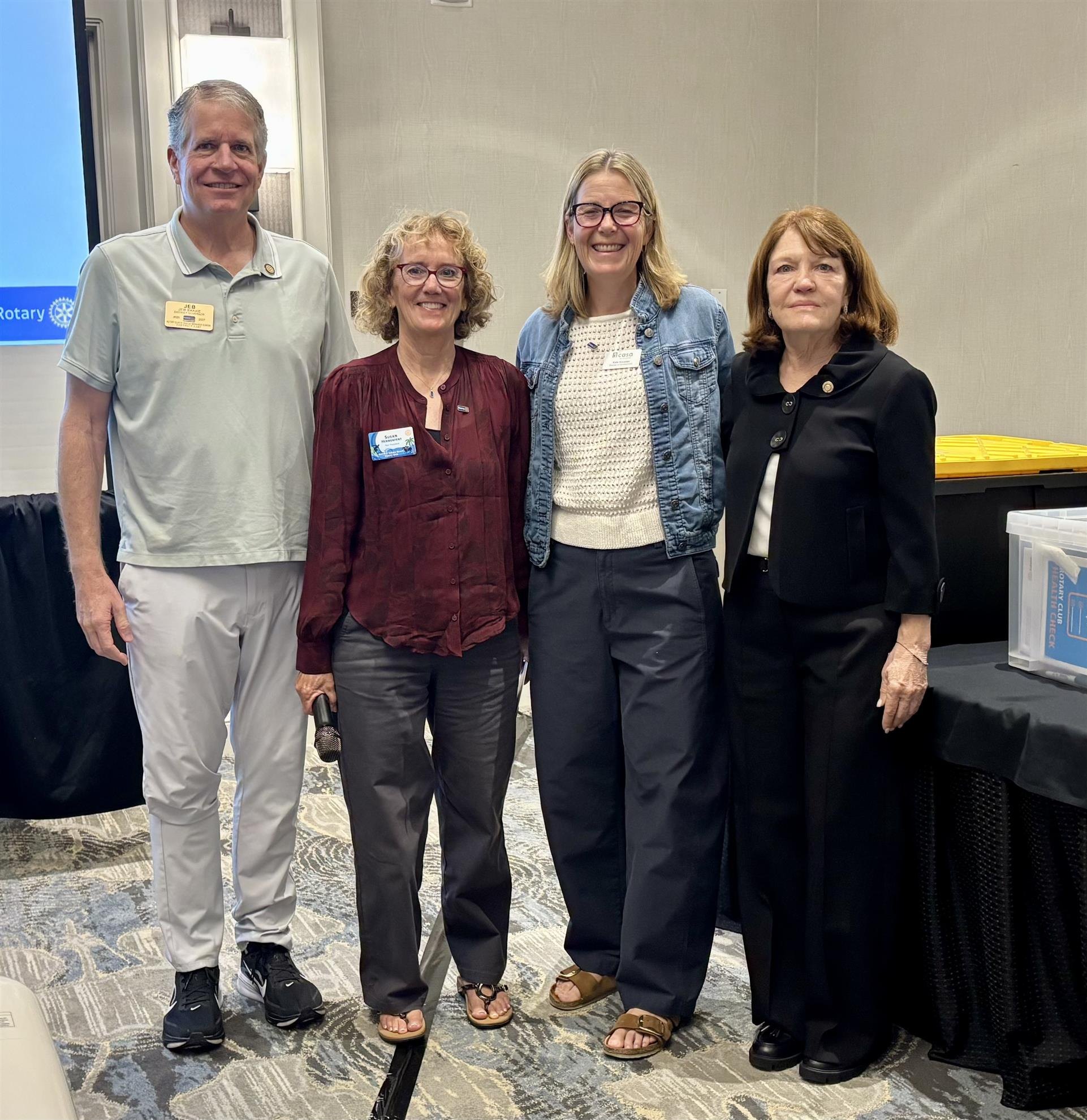 Four adults pose together indoors in front of a Rotary Club banner.