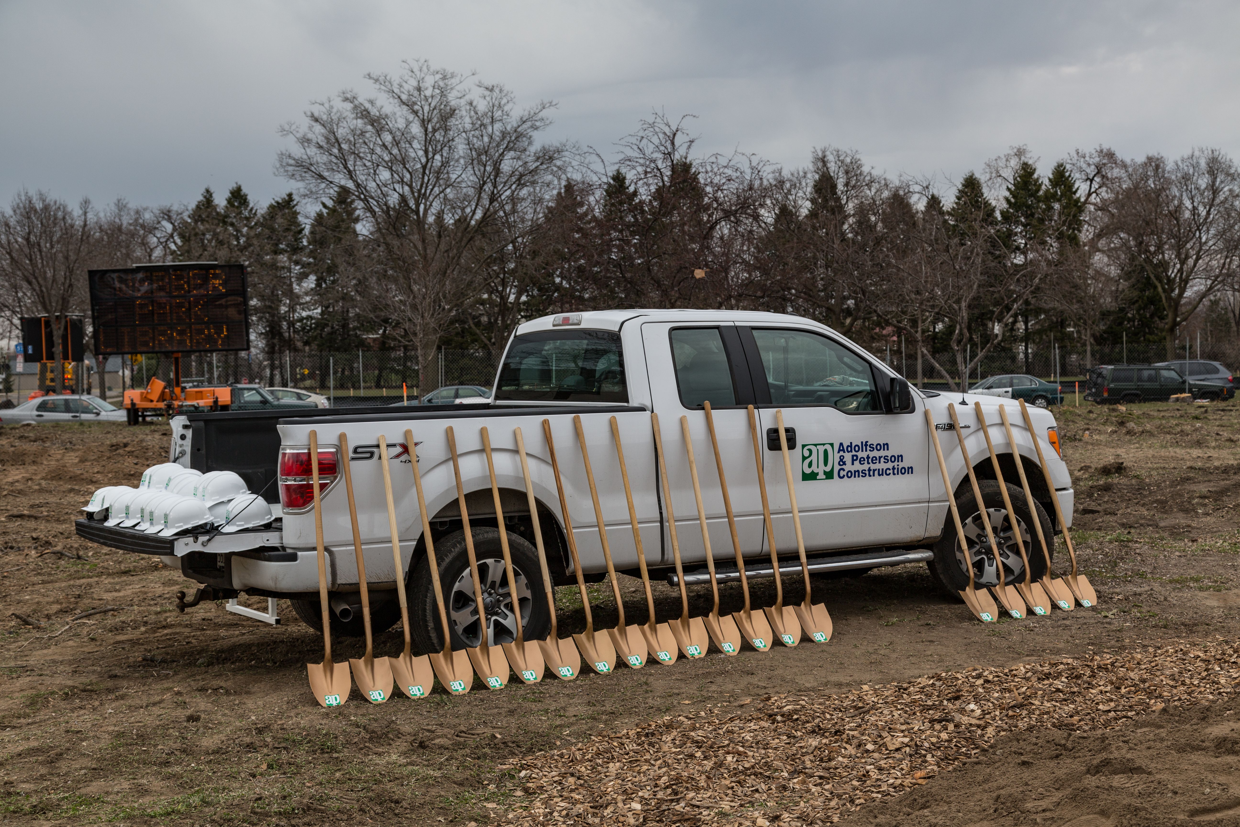 Several ceremonial golden shovels leaning against a white pickup truck on a dirt lot.