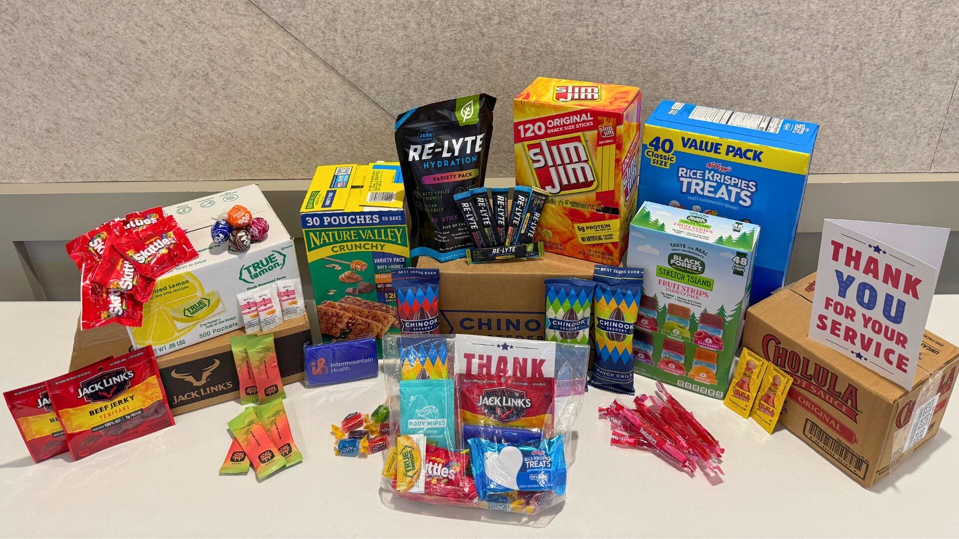Assorted packaged snacks and a thank-you sign arranged on a table beside a cardboard shipping box.