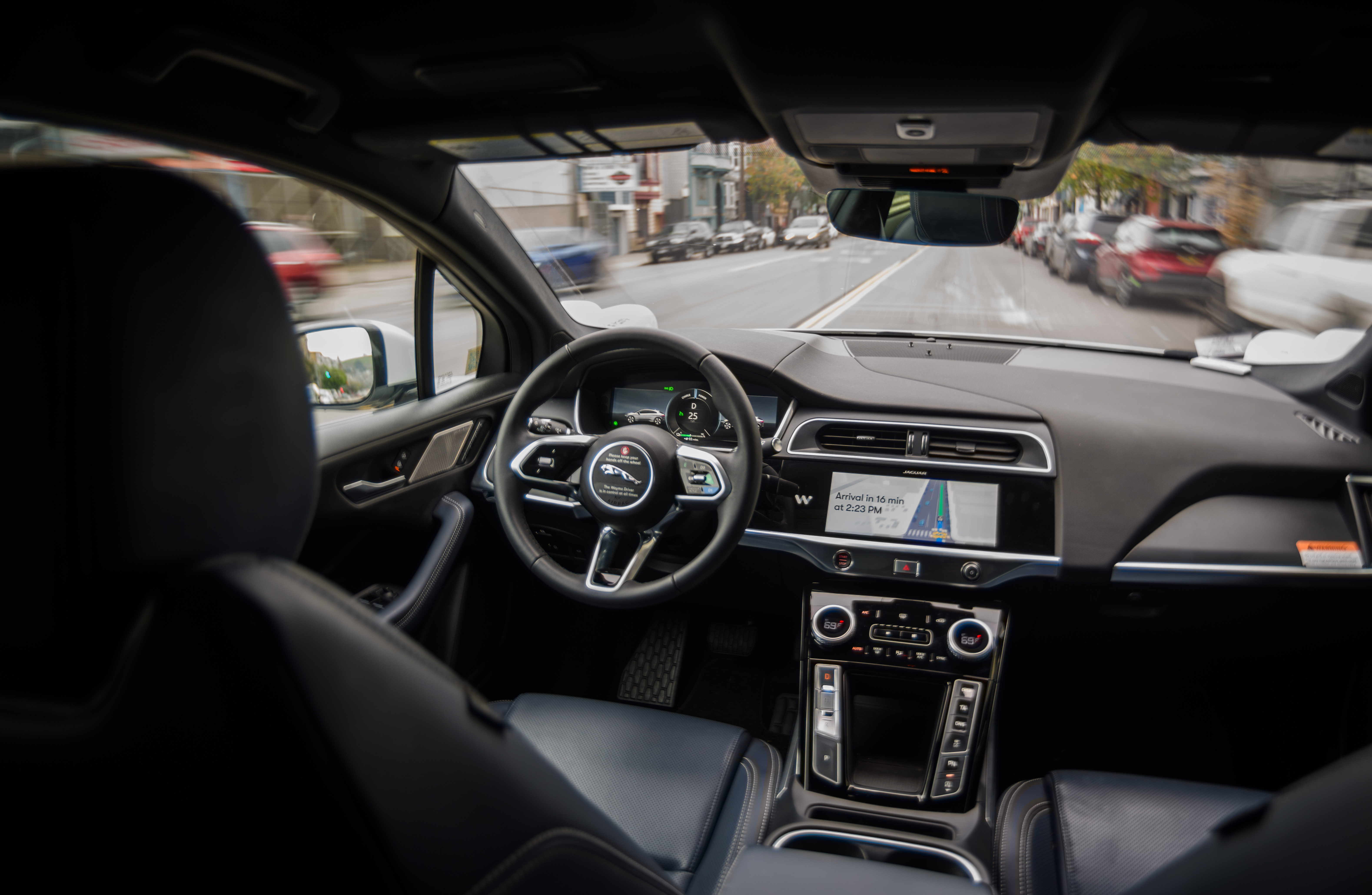 Empty driver's seat inside a moving driverless robotaxi with city street ahead.