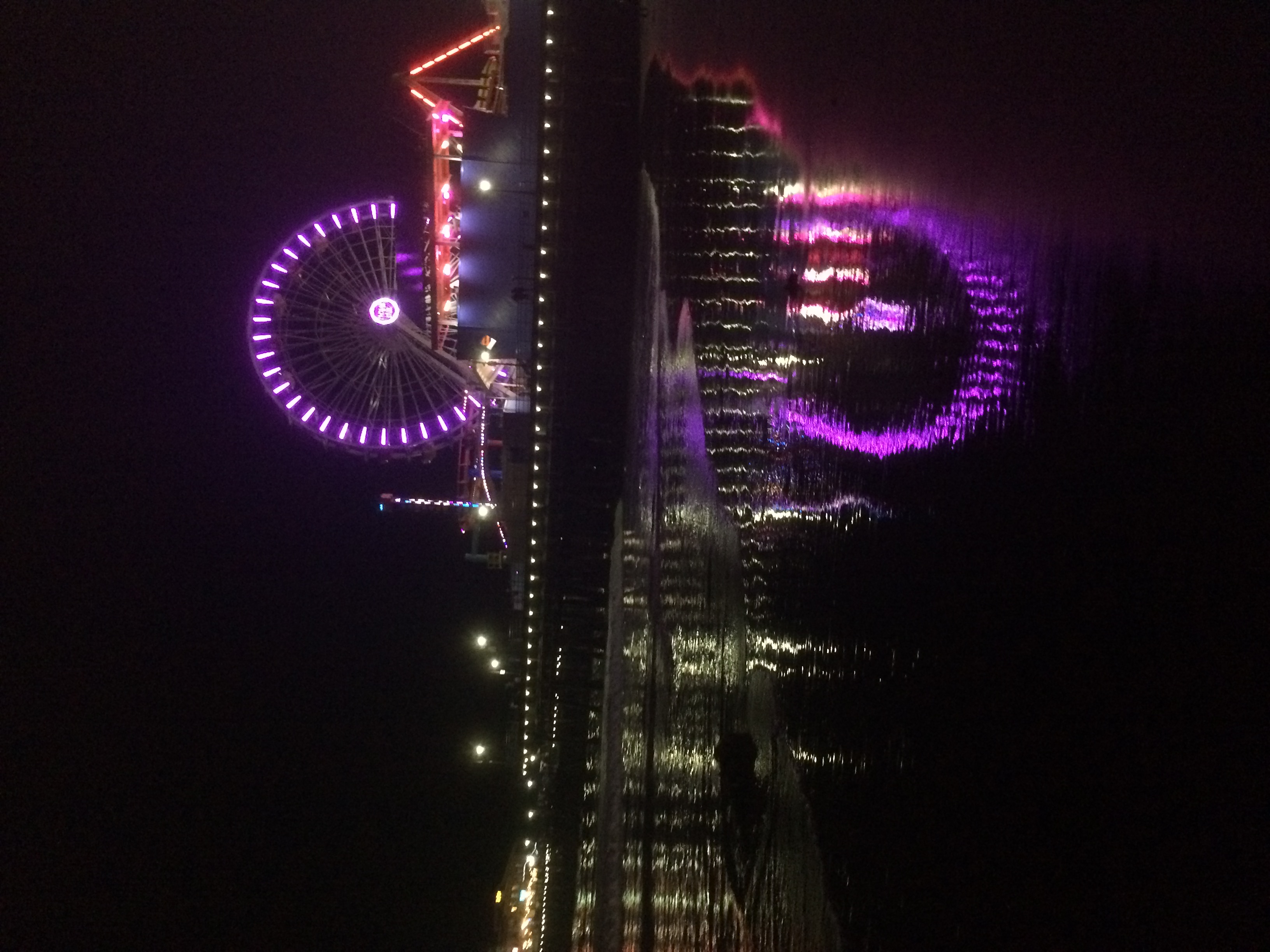 Ferris wheel glowing with colorful LED lights on a pier at night, reflections on wet sand
