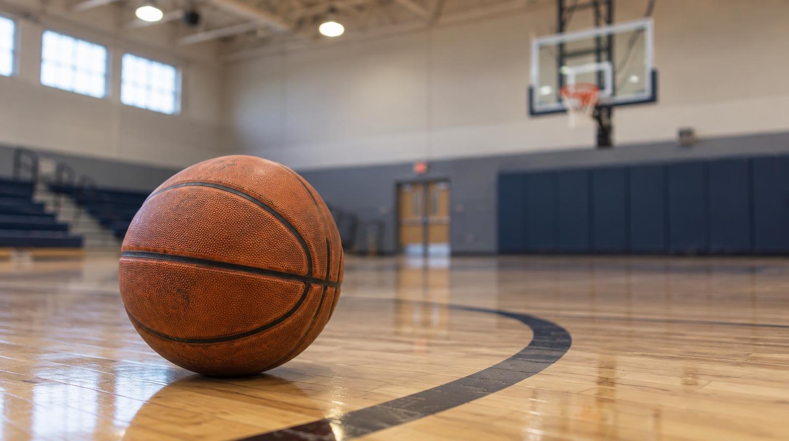 A basketball resting on a hardwood gym floor near a three-point arc.