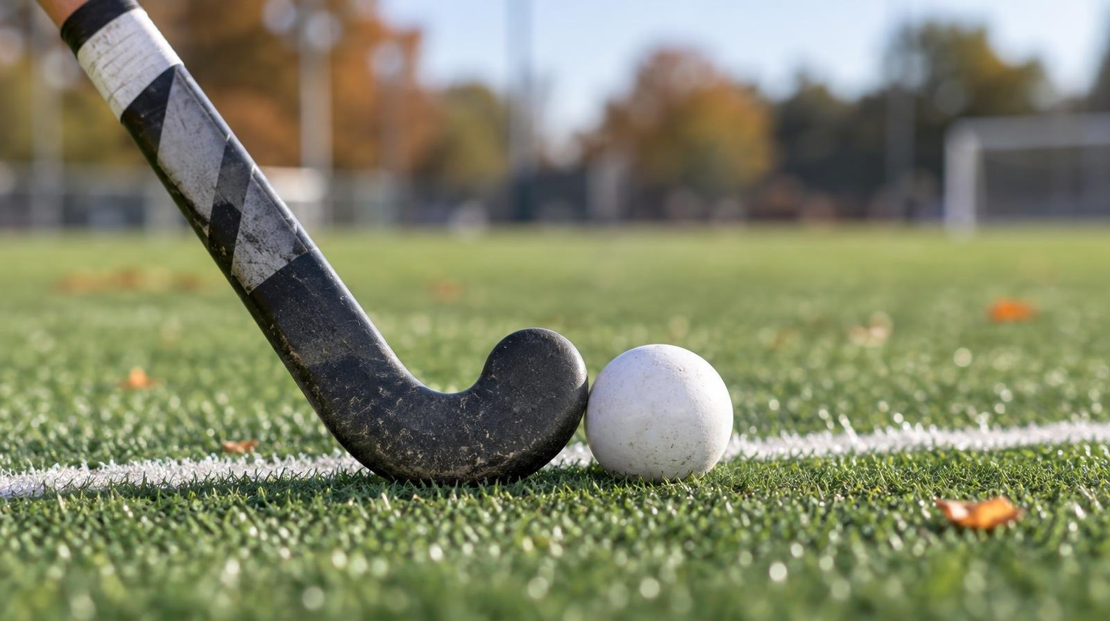 A field hockey stick and ball resting on green artificial turf near a white line.