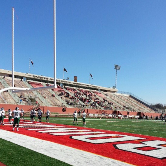 Stadium field with Cardinals end zone markings and grandstands visible under a clear sky.