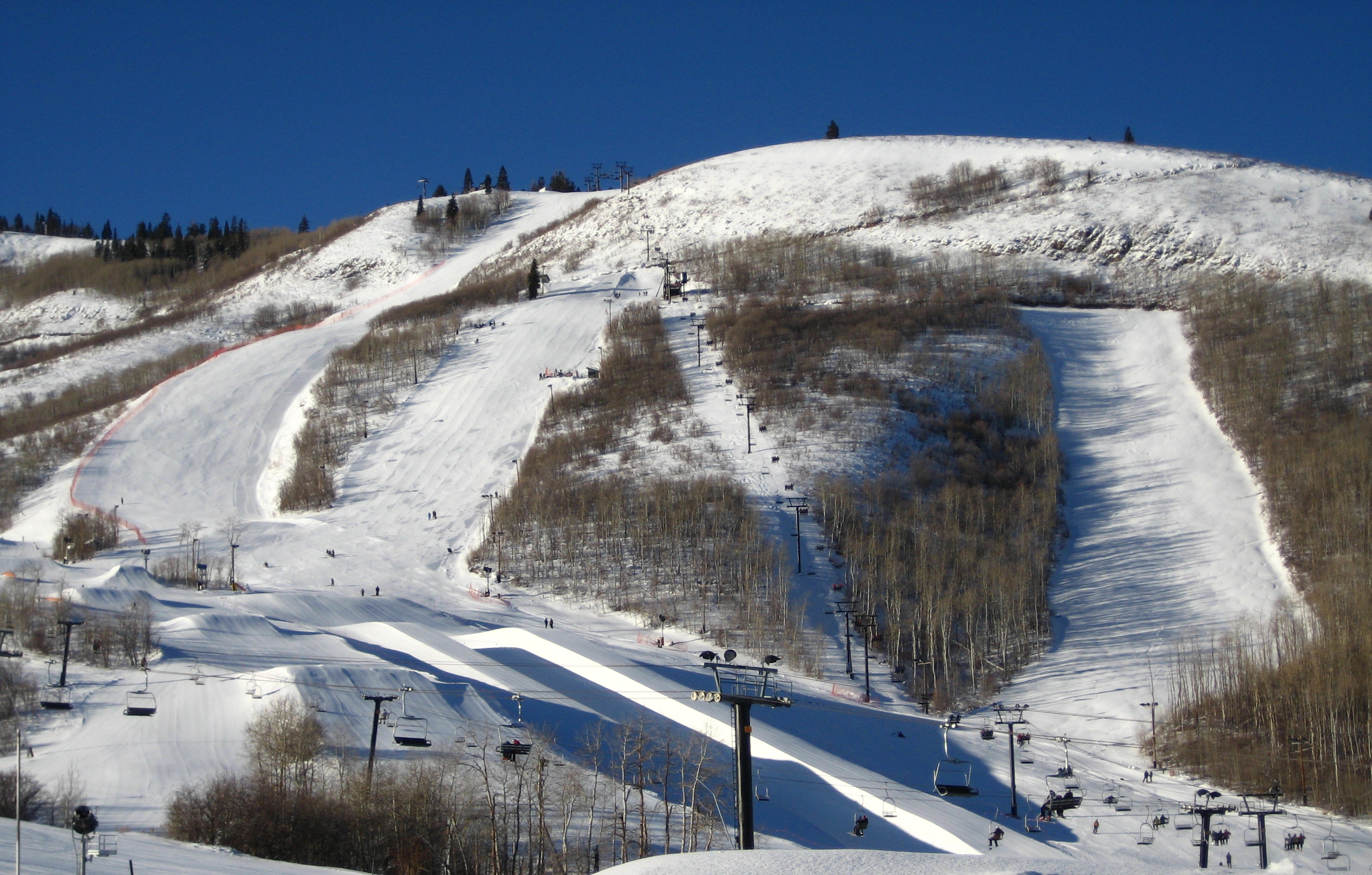 Snow-covered ski slopes and chairlifts on a hillside under a clear blue sky.