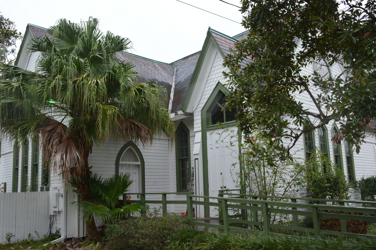 White Victorian wooden chapel with Gothic windows and a palm tree in the foreground
