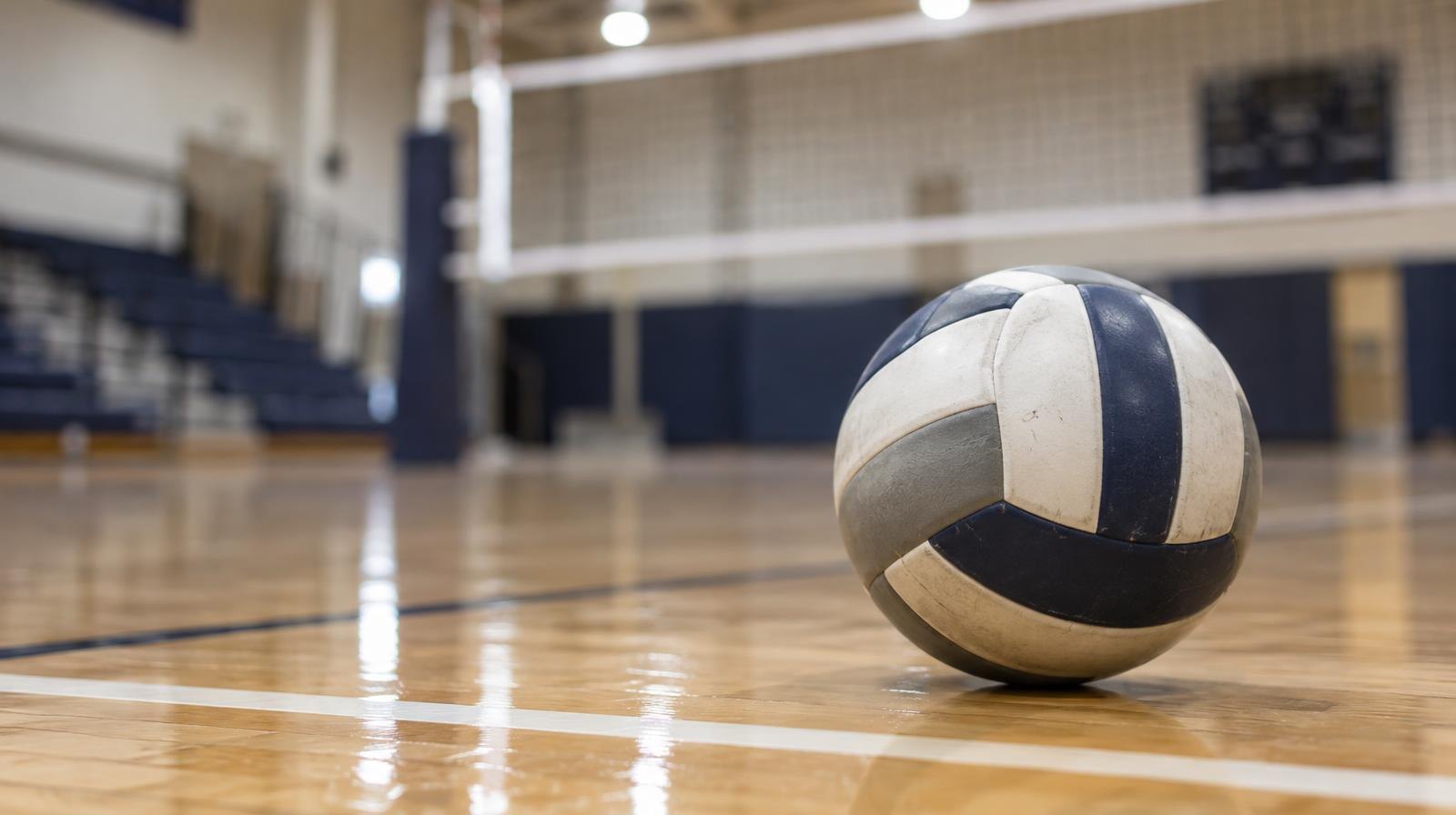 A volleyball resting on a hardwood gymnasium floor near the net.