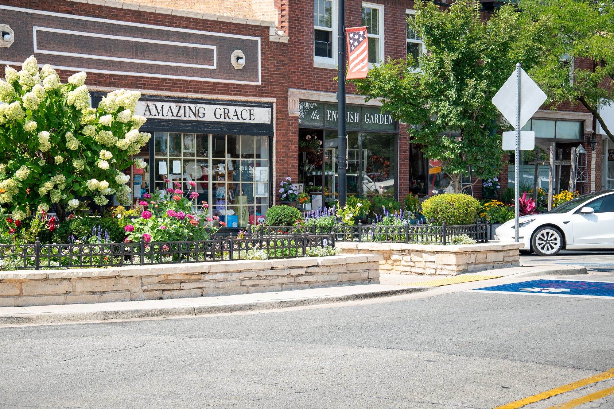 Brick storefronts with colorful flower planters along a sunny small-town downtown street.