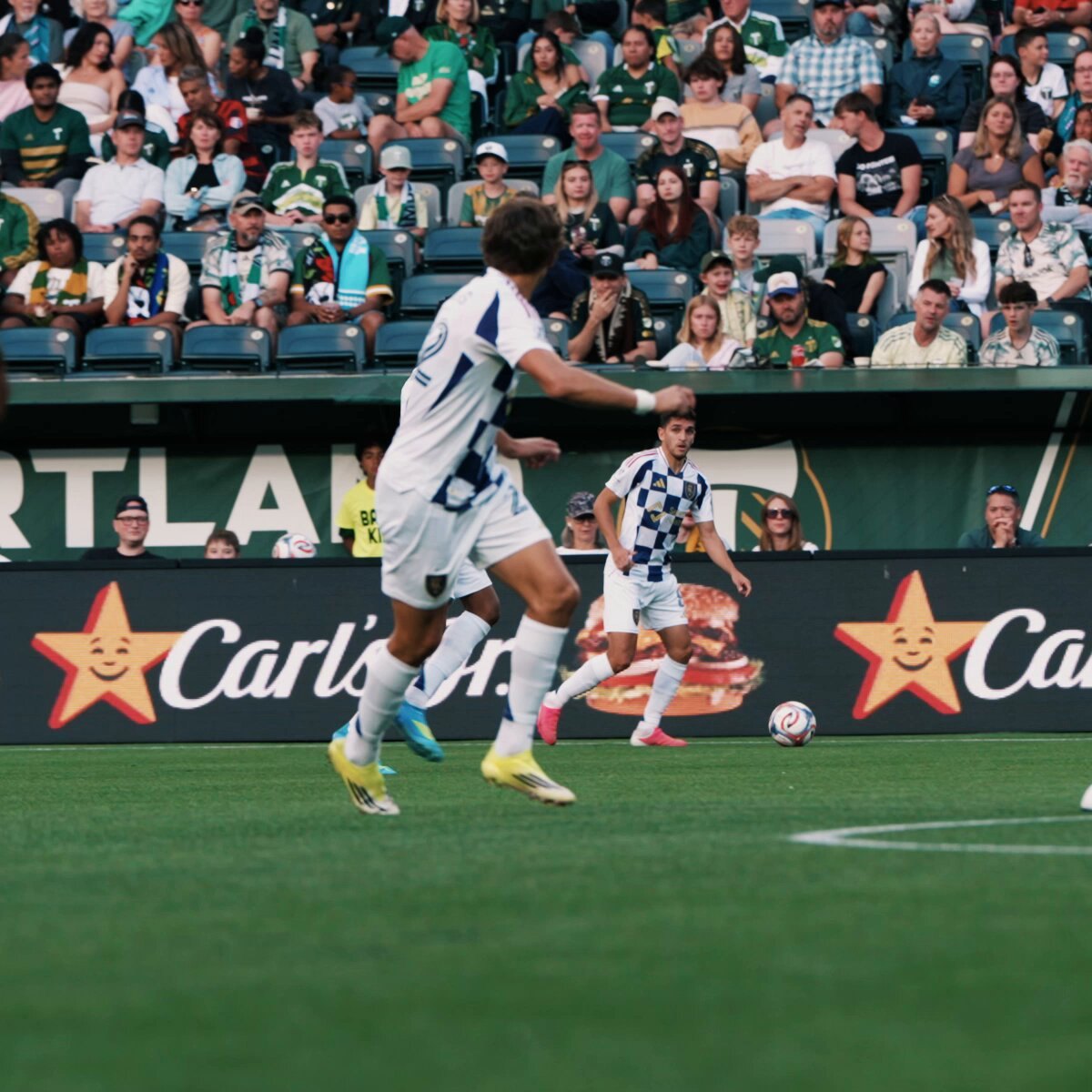 Two soccer players in white uniforms compete near the sideline during a match.