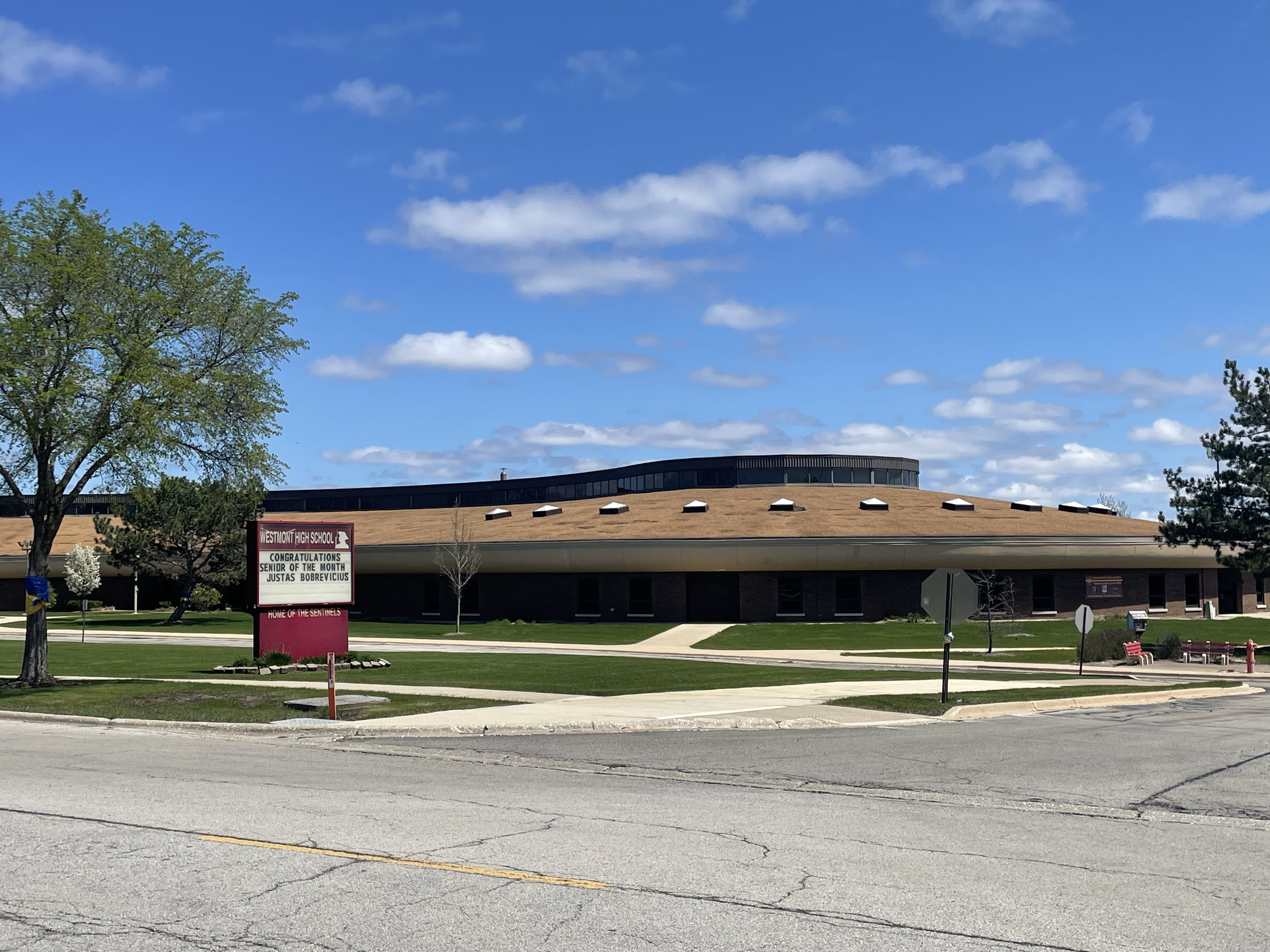 Brick school building exterior with marquee sign, green lawn, and blue sky.