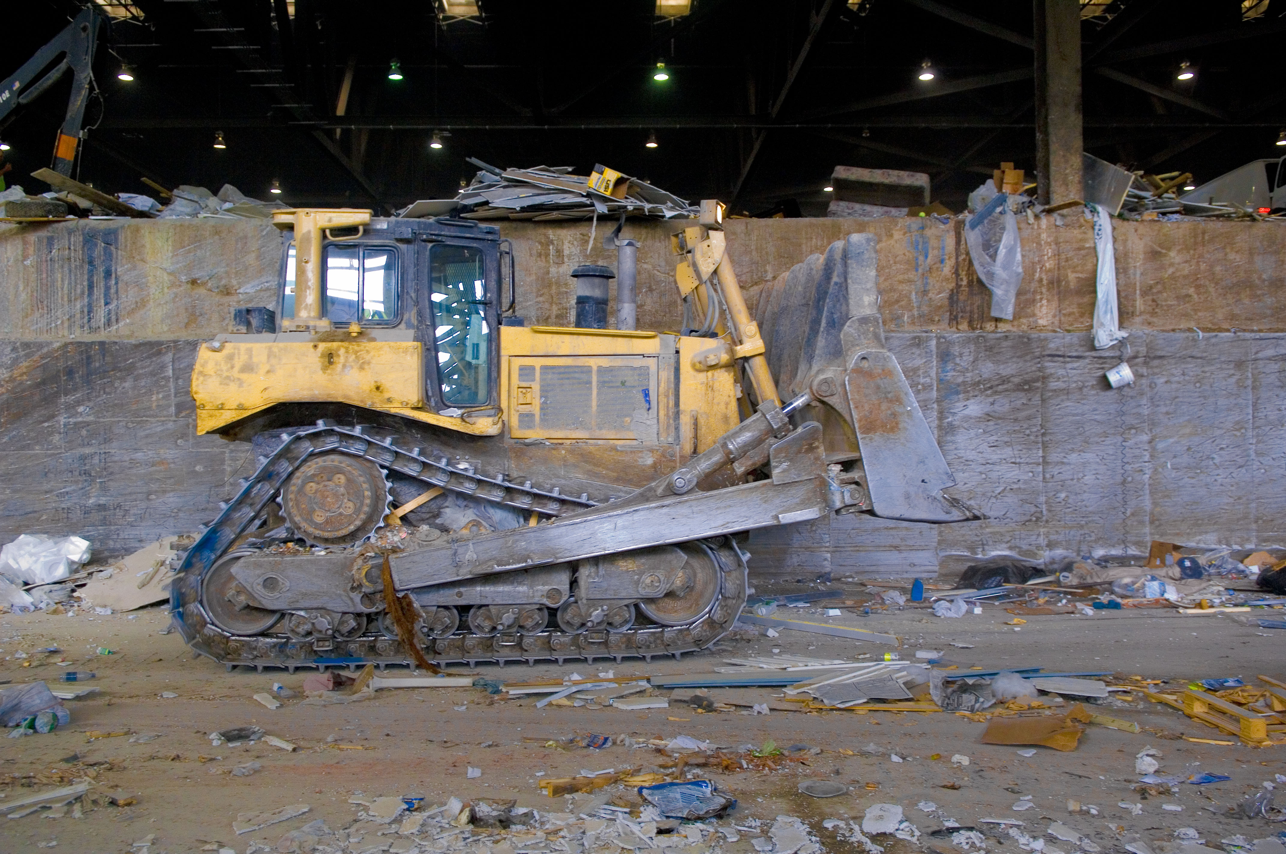 Yellow bulldozer pushing refuse inside a large industrial waste facility.