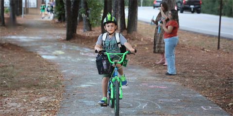 Young child wearing a helmet rides a green bicycle on a paved pathway.