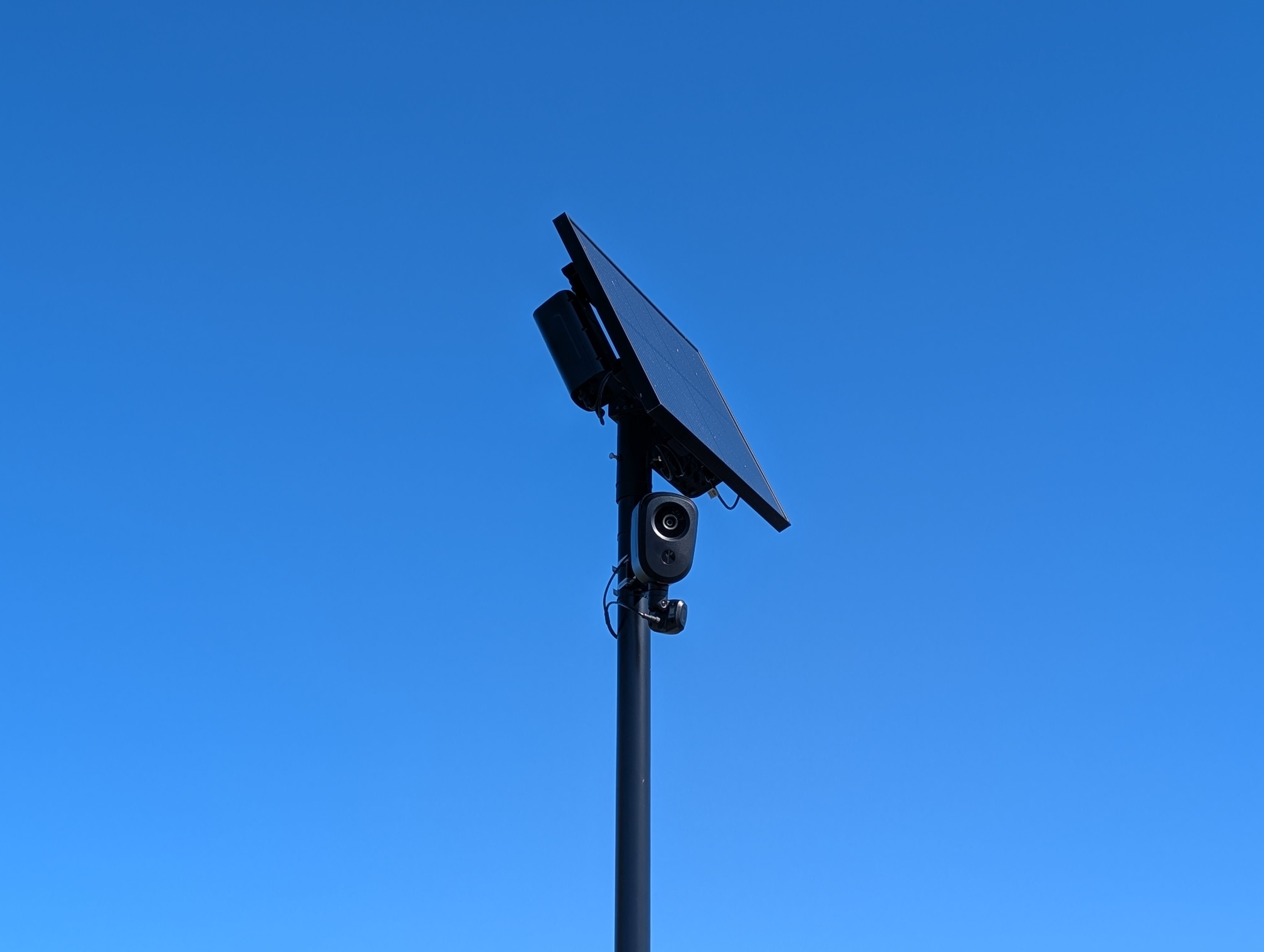 A pole-mounted Flock Safety ALPR camera with a solar panel photographed against a blue sky.