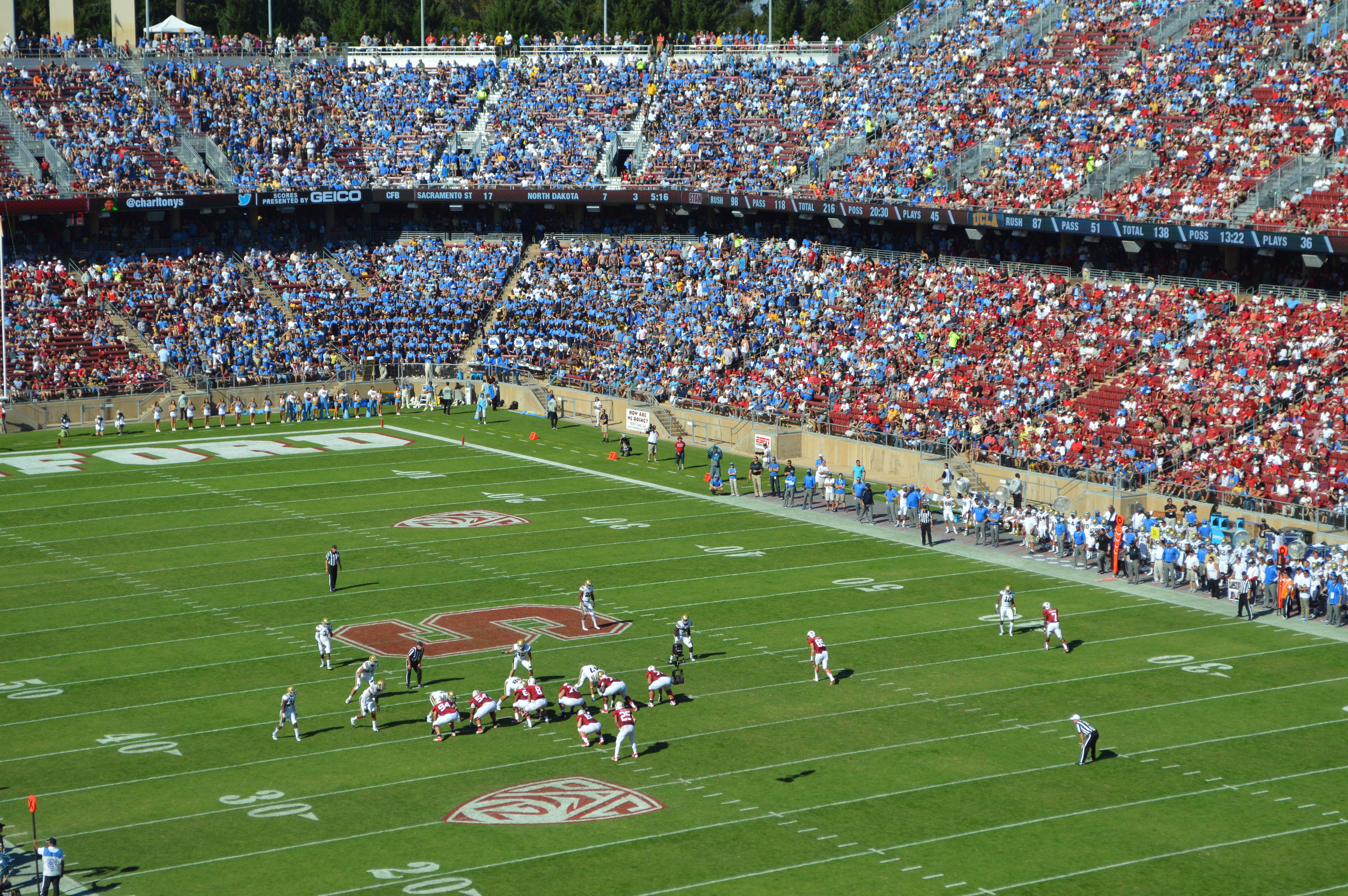 College football players on the field at Stanford Stadium with fans in the stands.
