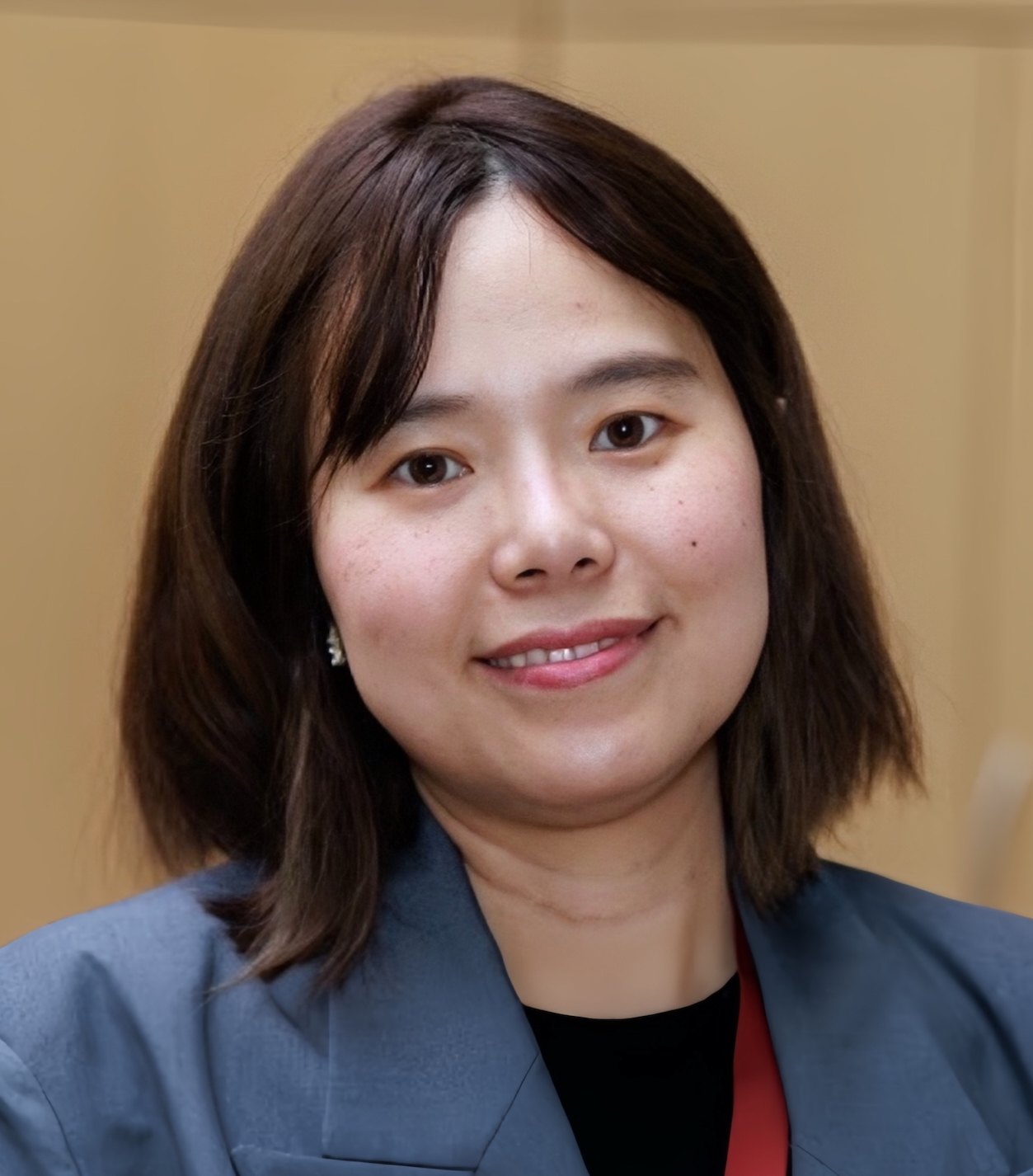 Woman in a gray blazer smiling in a professional portrait against a beige background.